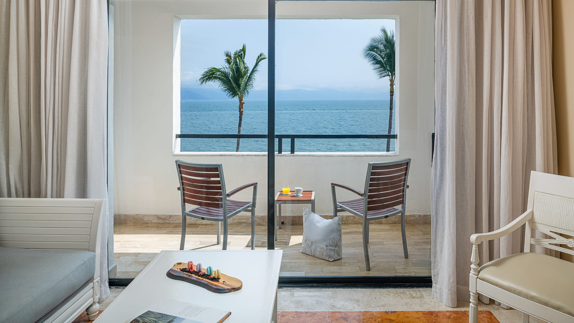 Ocean view hotel suite balcony with tropical palm trees and outdoor seating.