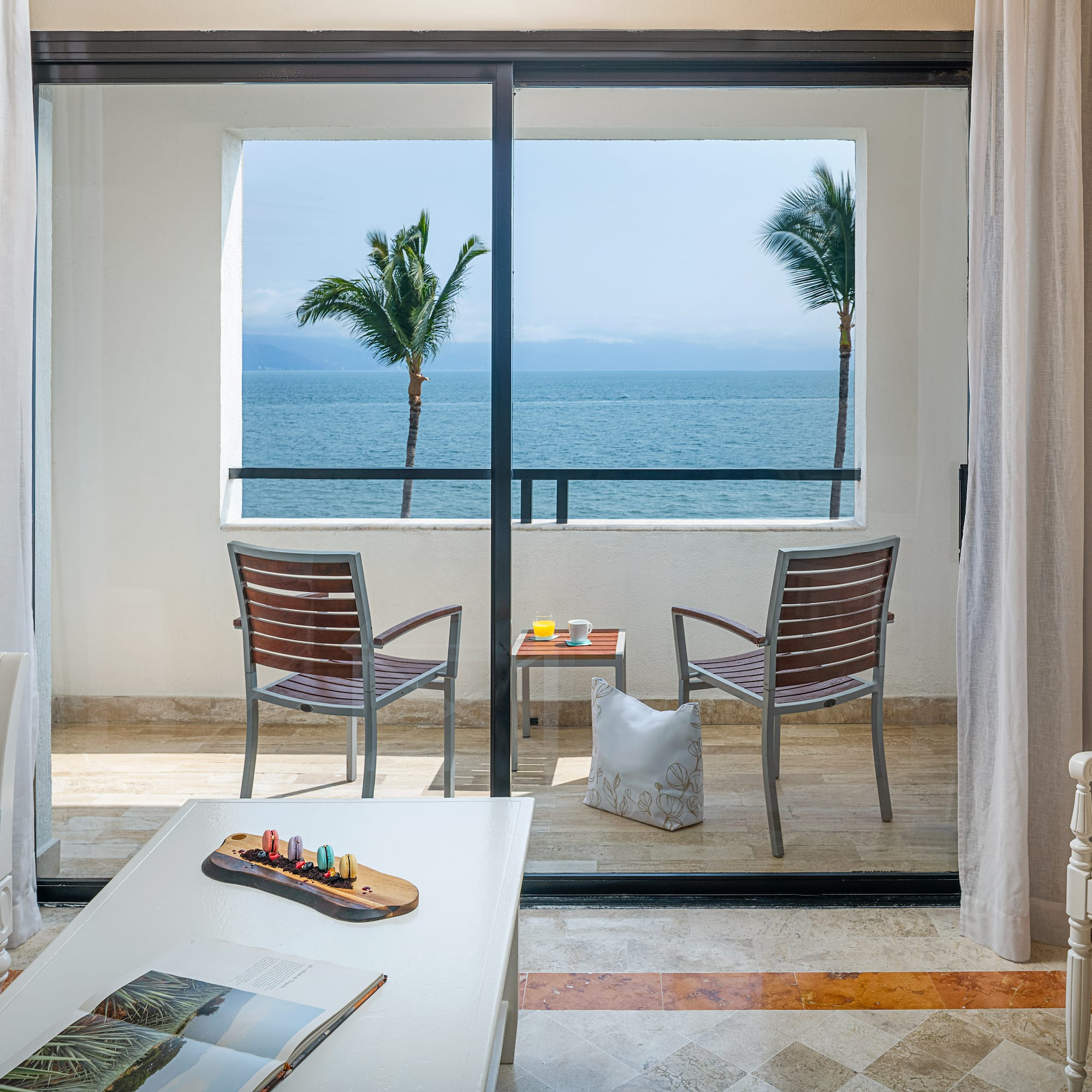 Ocean view hotel suite balcony with tropical palm trees and outdoor seating.