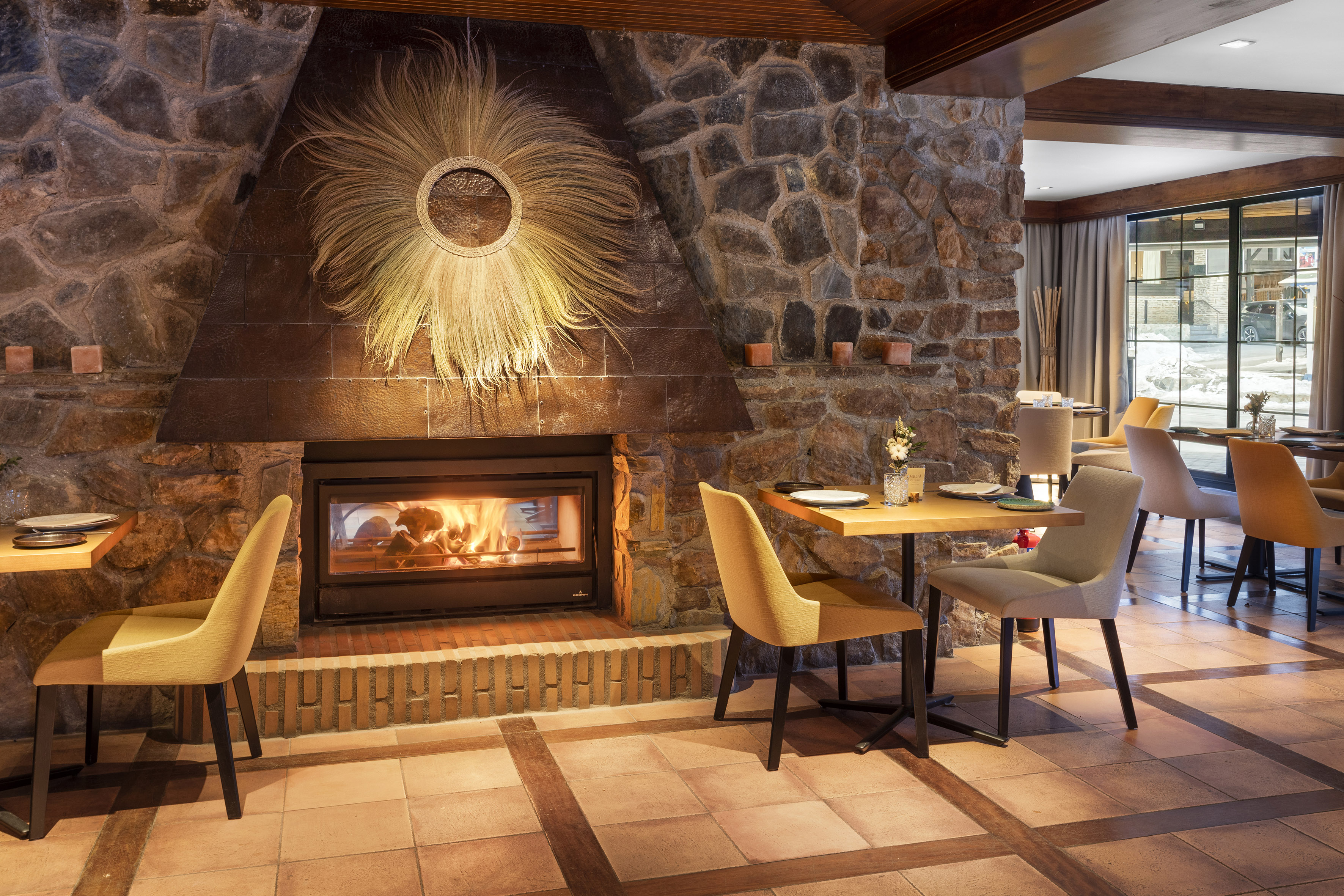 Cozy restaurant with rustic stone fireplace, burning fire, and dining tables.
