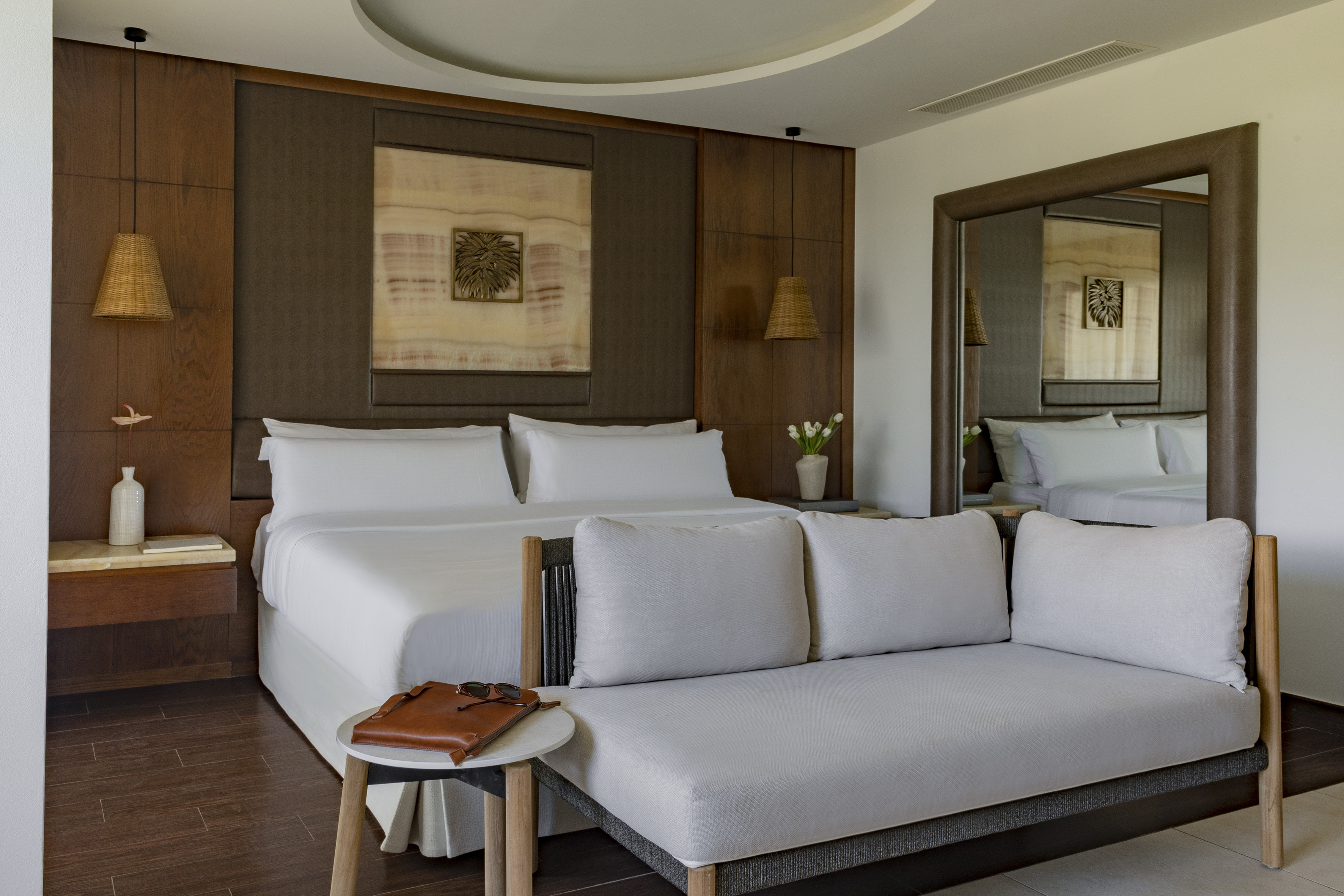 Chic bedroom with king bed, wooden headboard, rattan lights, and lounge sofa.