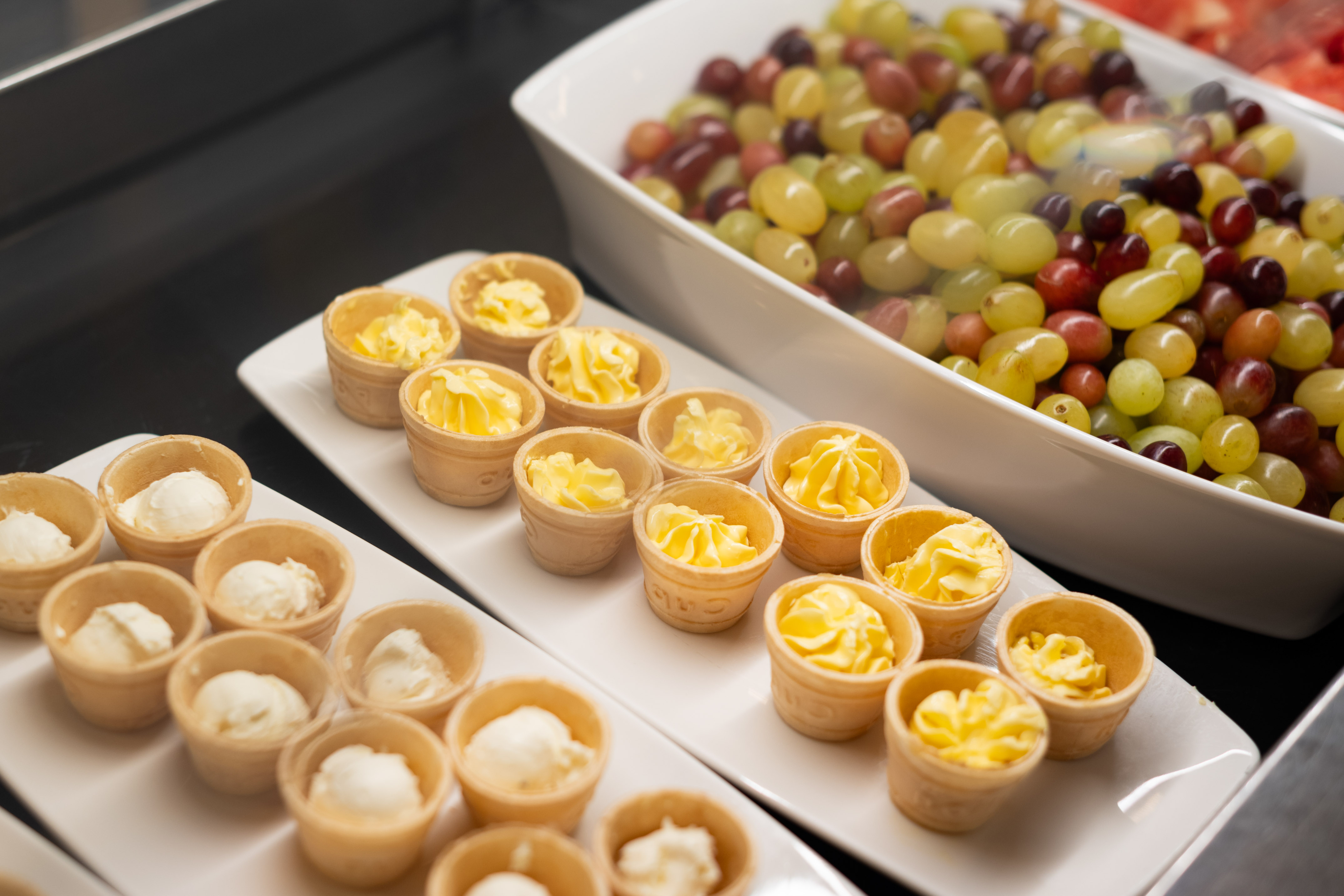 Mini waffle cups with butter and cream, mixed grapes on a breakfast buffet.