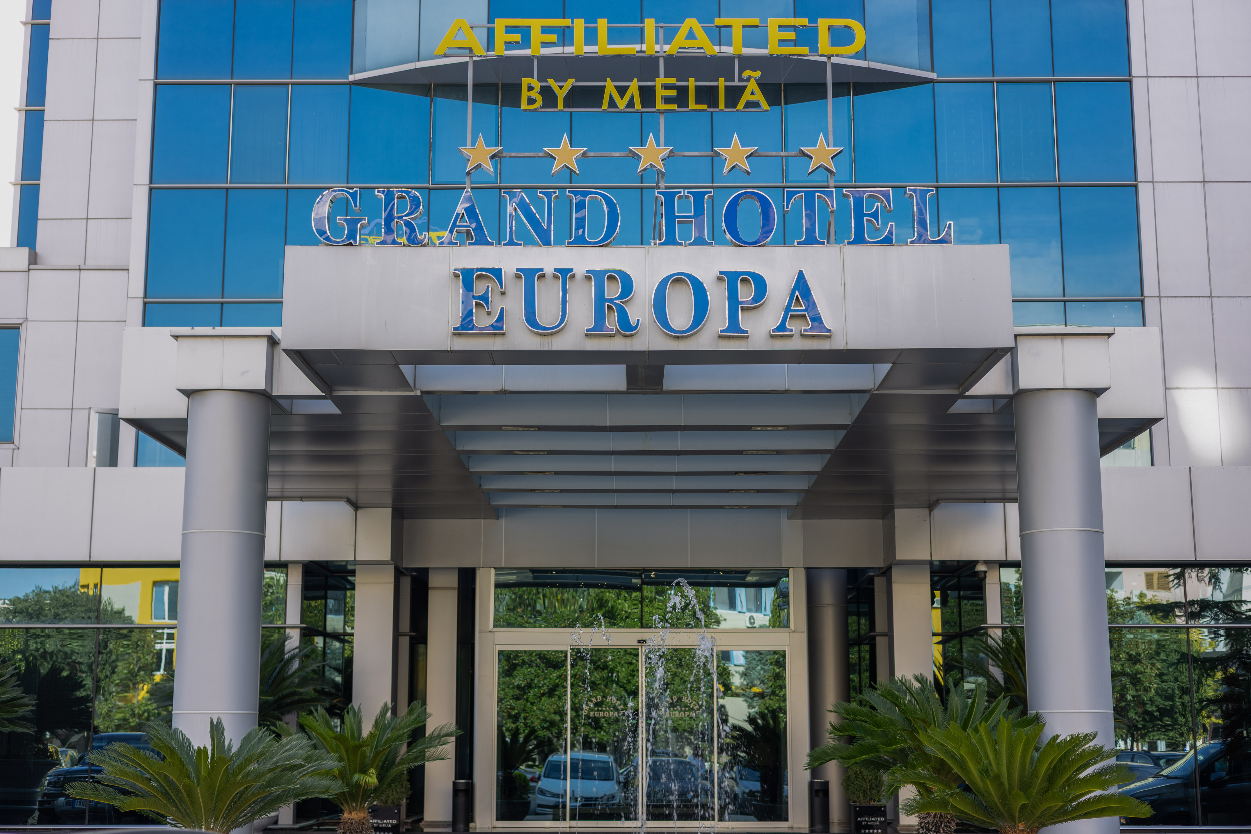 Grand Hotel Europa by Melià entrance with 5 stars, blue glass facade and fountain.