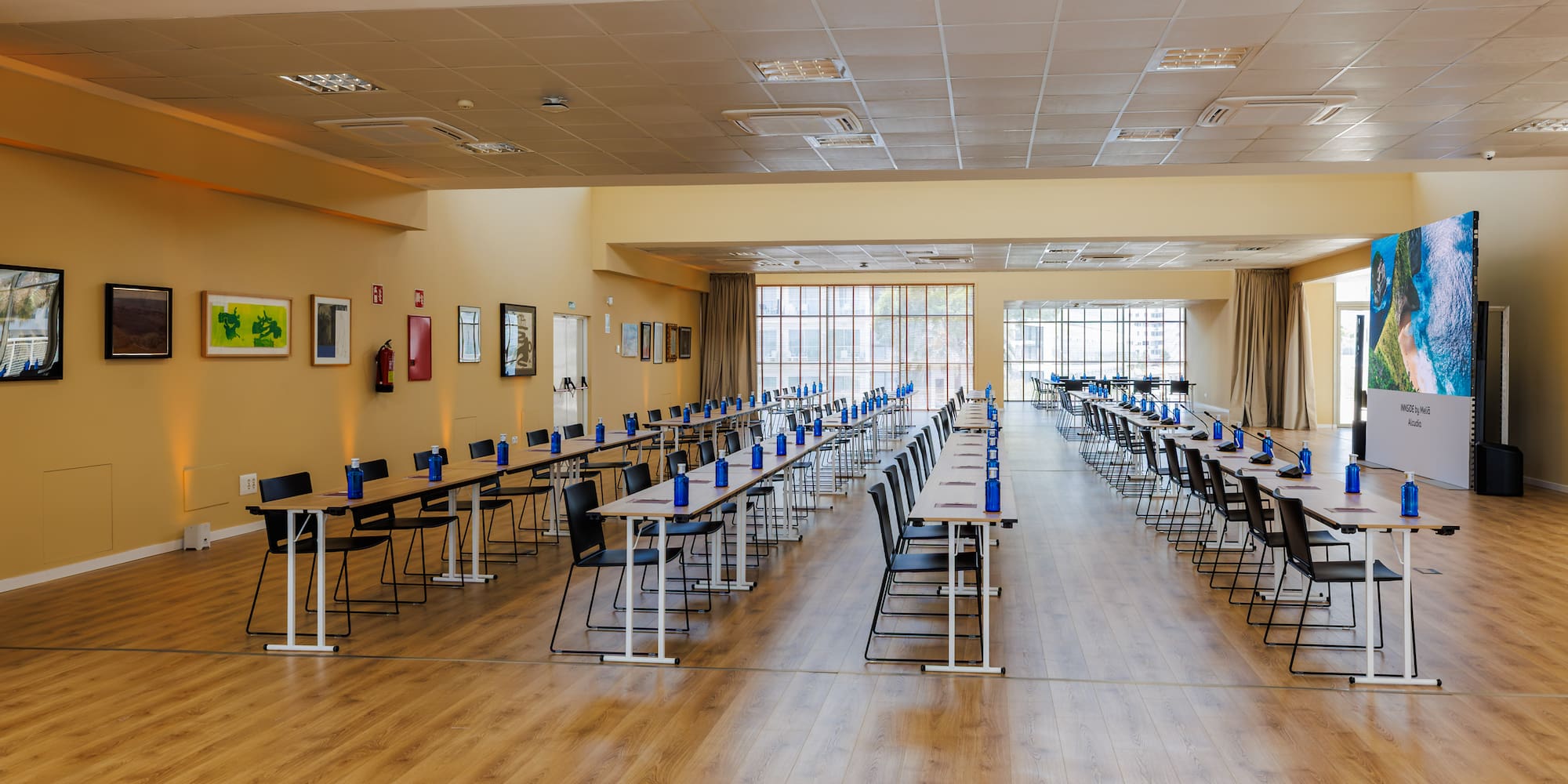 Bright, modern conference room with tables, chairs, and large screen for events.