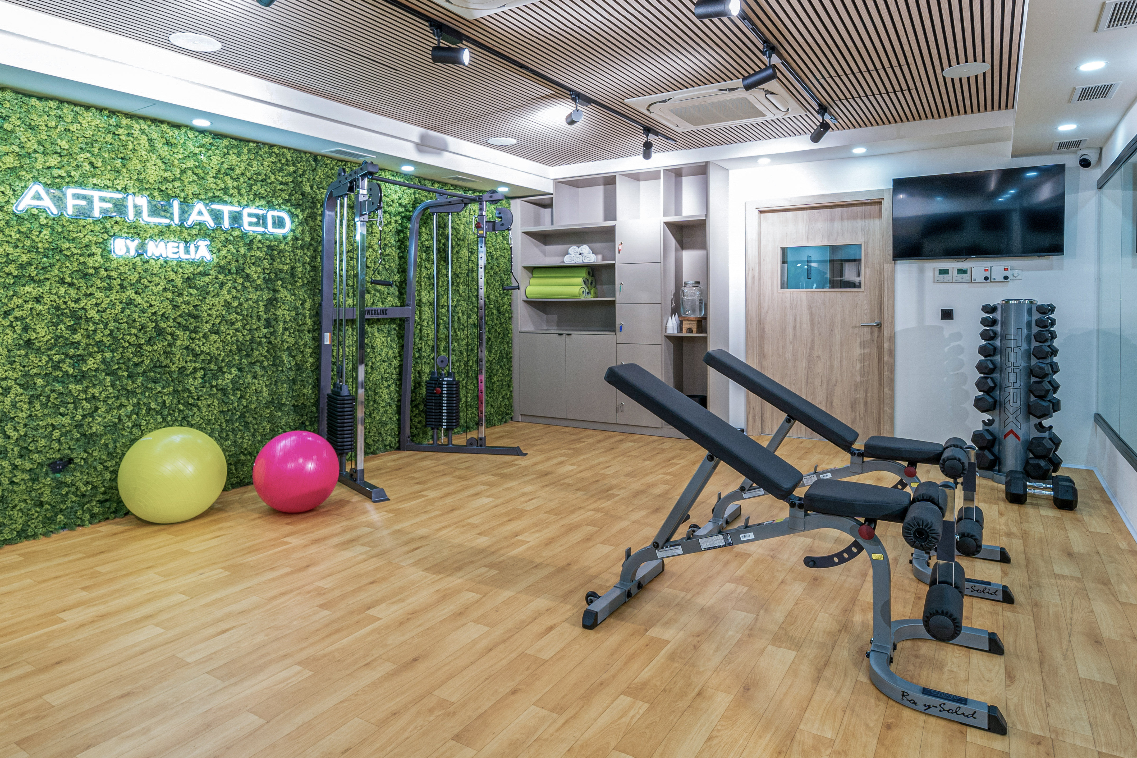 Modern Melia hotel gym with benches, dumbbells, cable machine, and green moss wall.