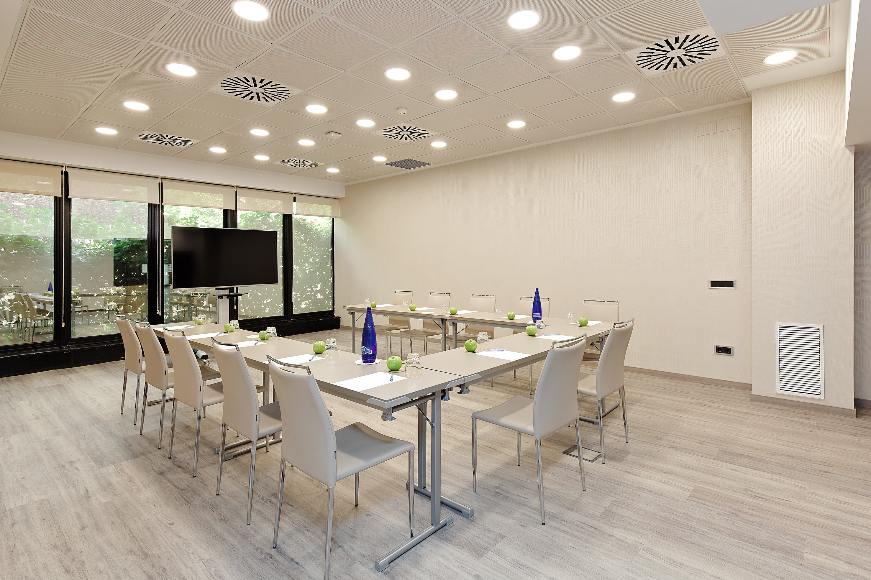 Modern conference room with U-shaped table, large TV screen, and bright windows.