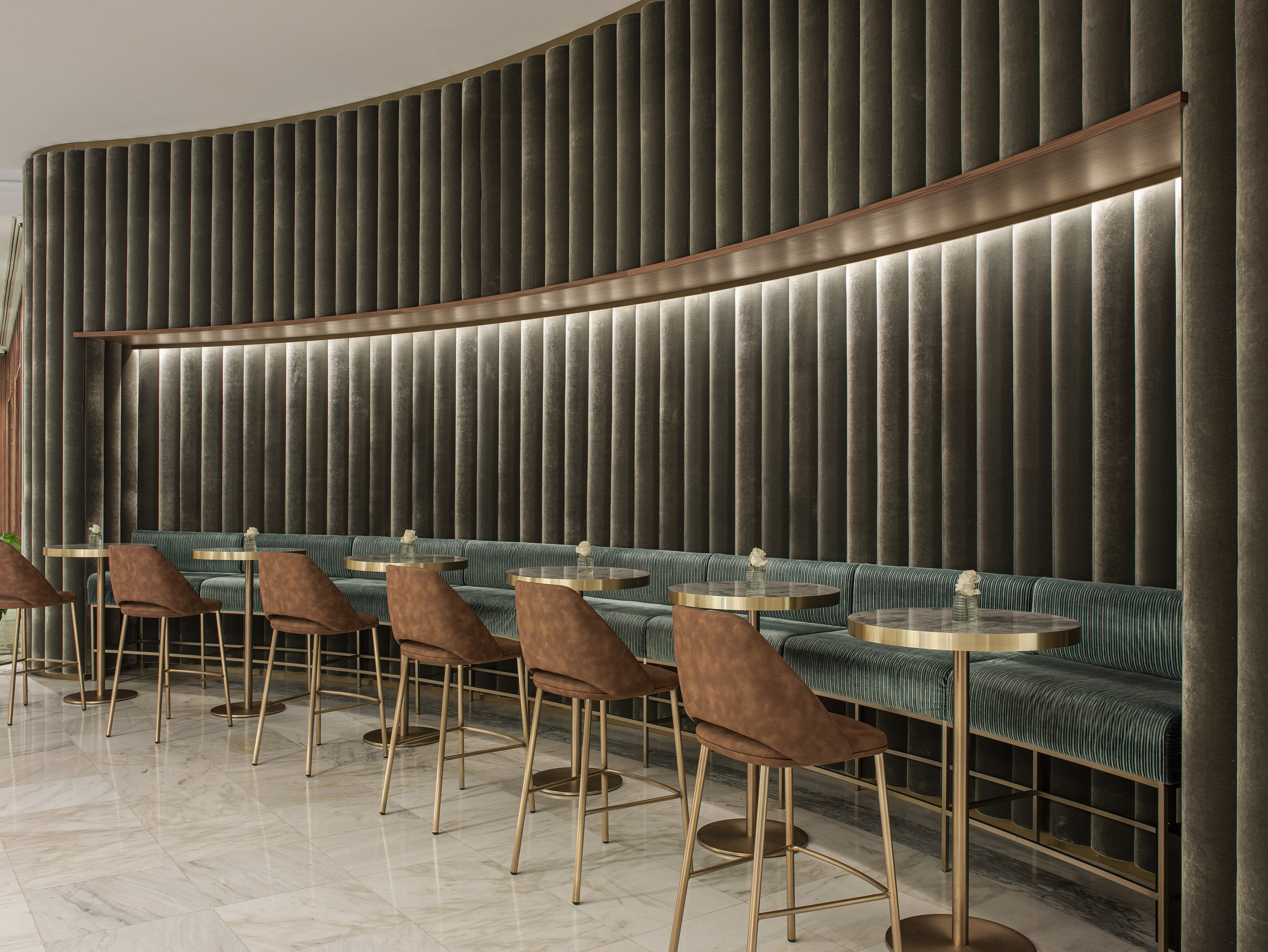 Modern lounge with curved velvet wall, green banquette seating, gold tables.