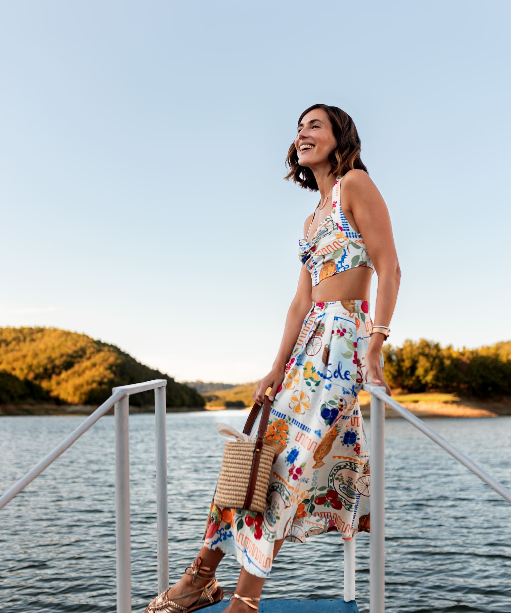 a woman in a skirt and top standing on a railing by water