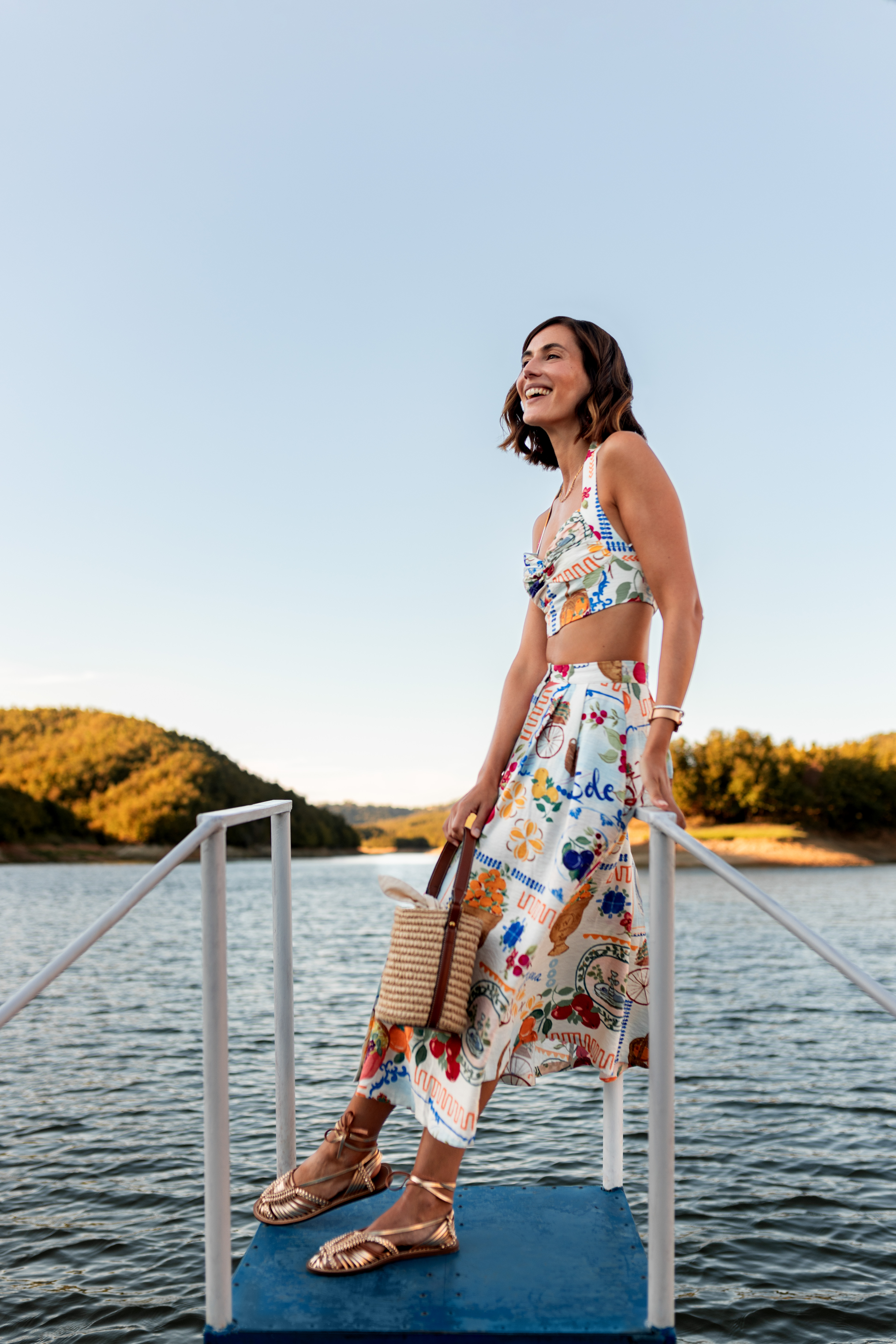 a woman in a skirt and top standing on a railing by water