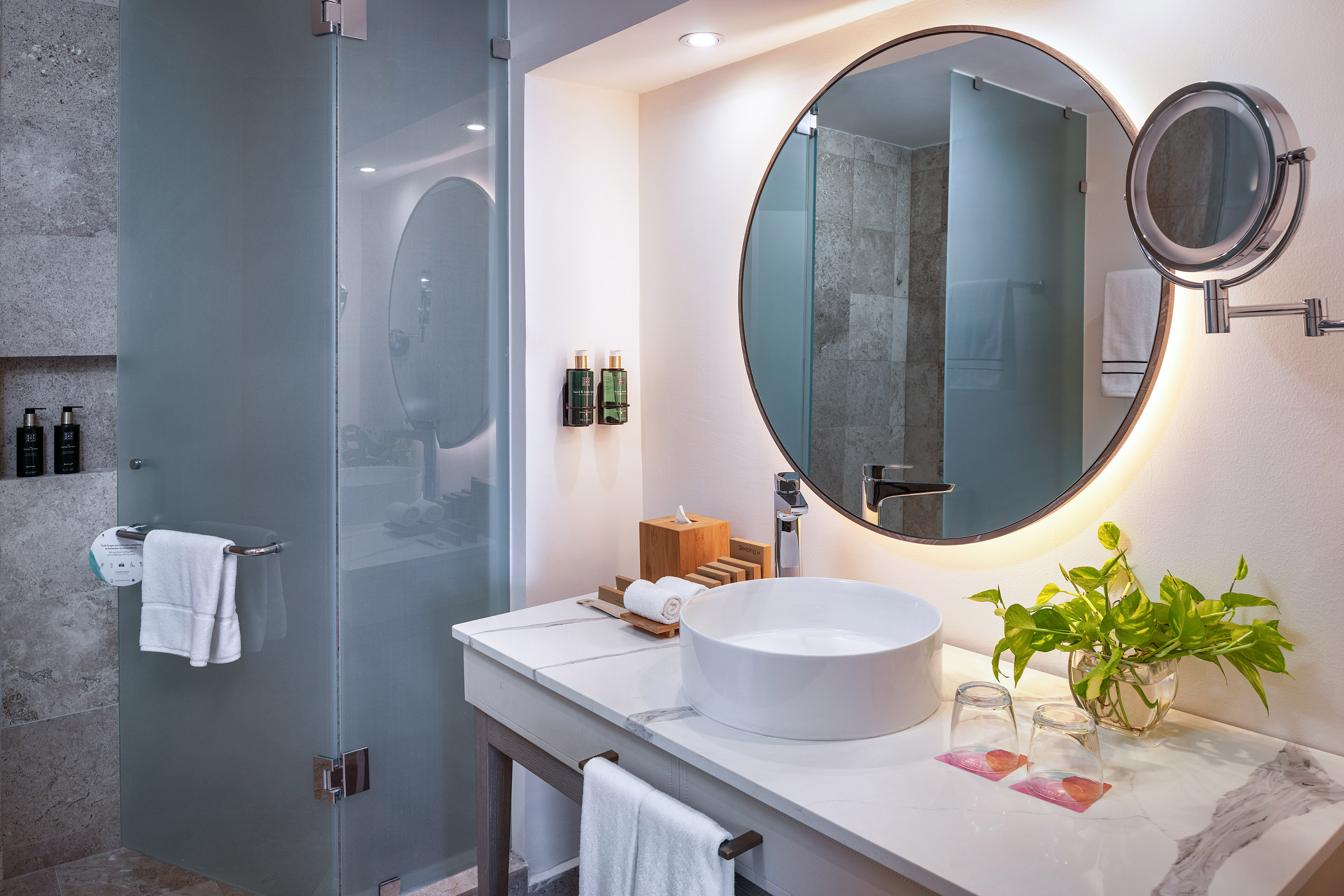 Modern hotel bathroom with round backlit mirror, vessel sink, and marble vanity.