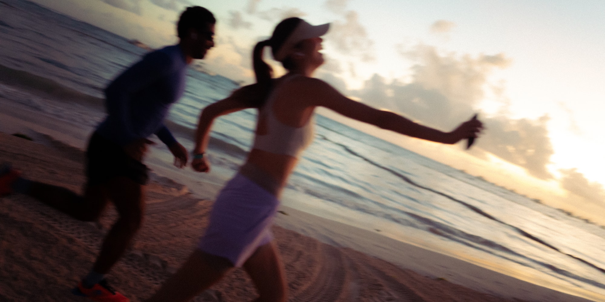 Man and woman jogging on sandy beach at sunset by the ocean.