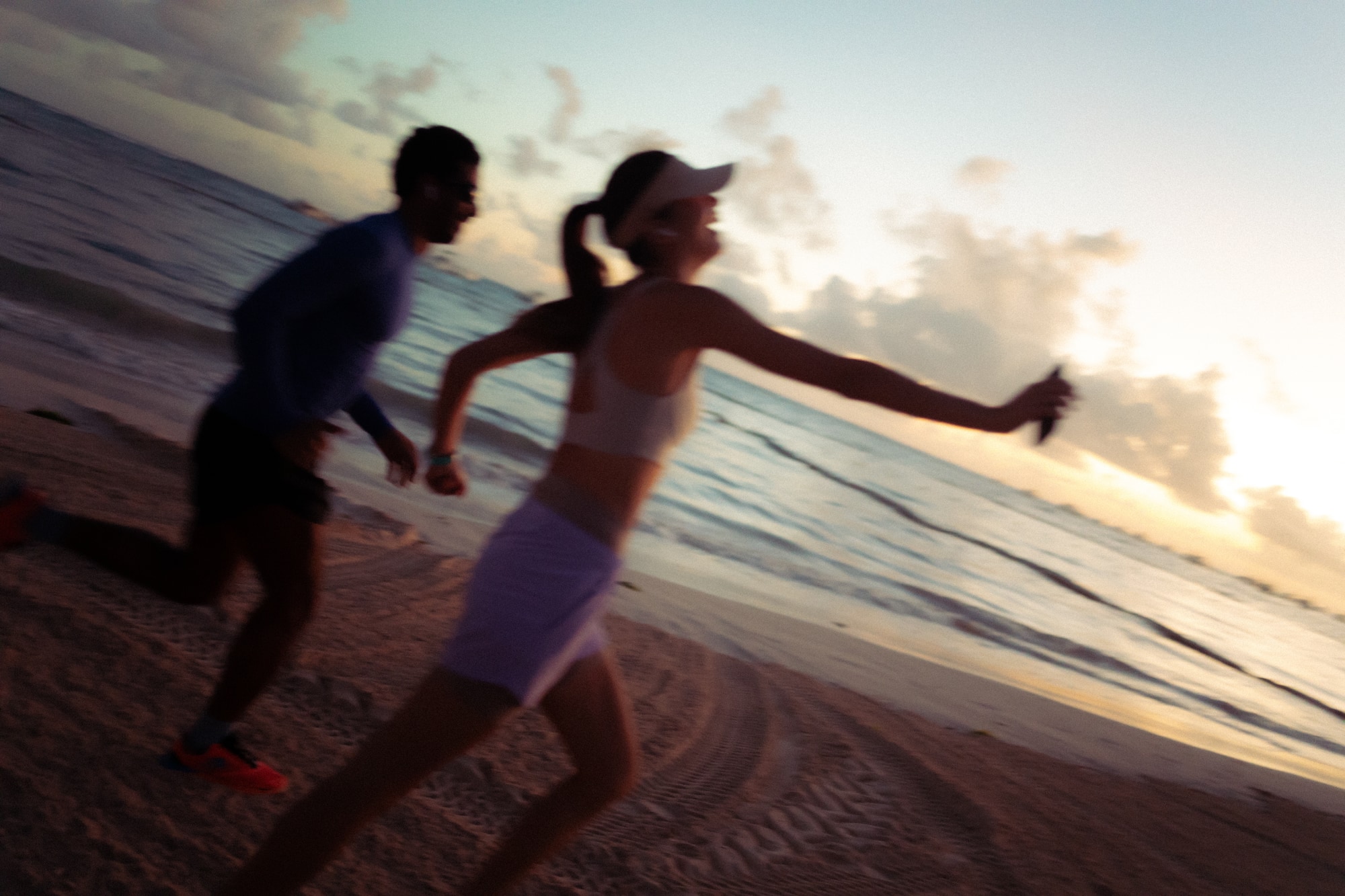 Runners on sandy beach at sunrise with ocean waves.