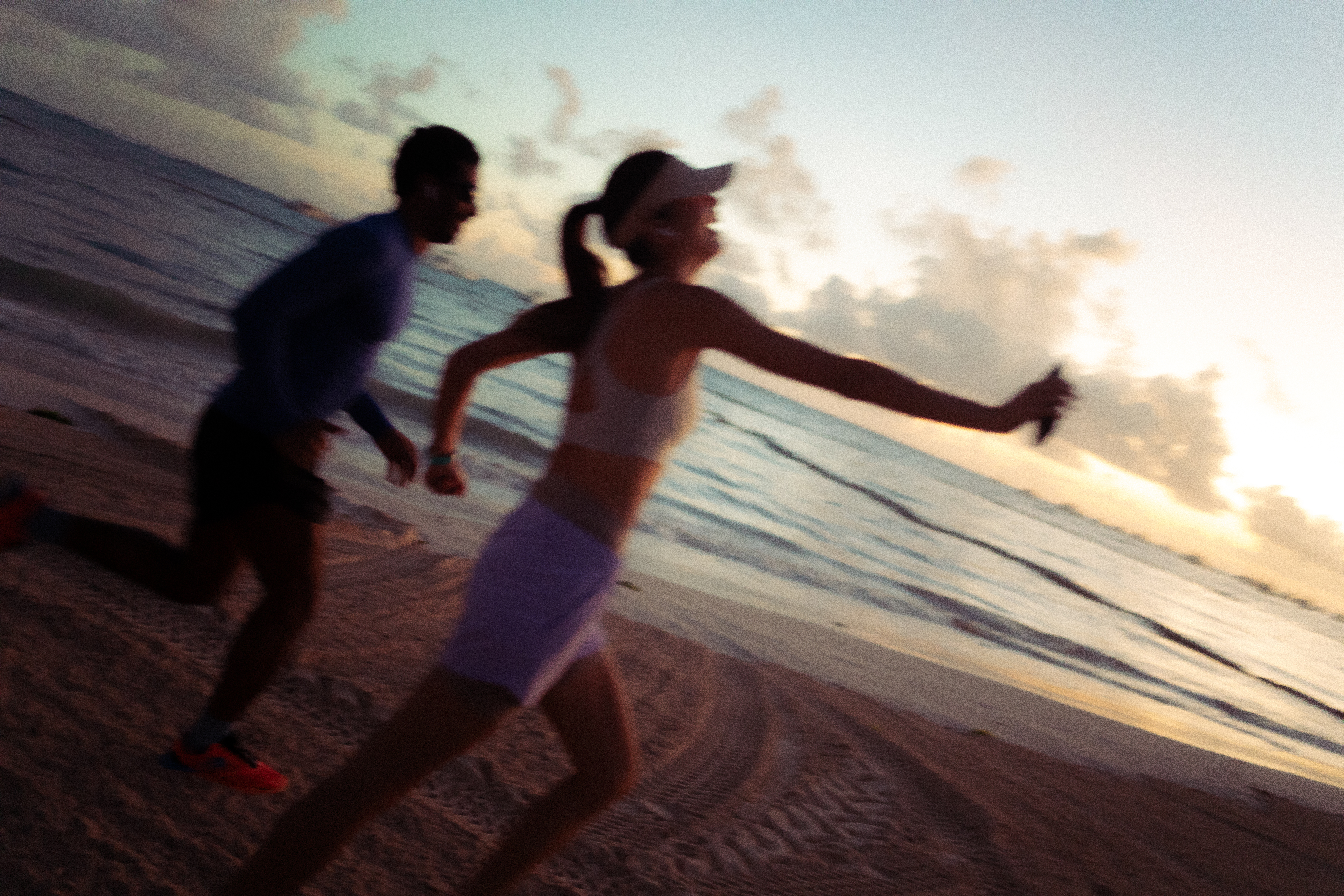 Runners on sandy beach at sunrise with ocean waves.
