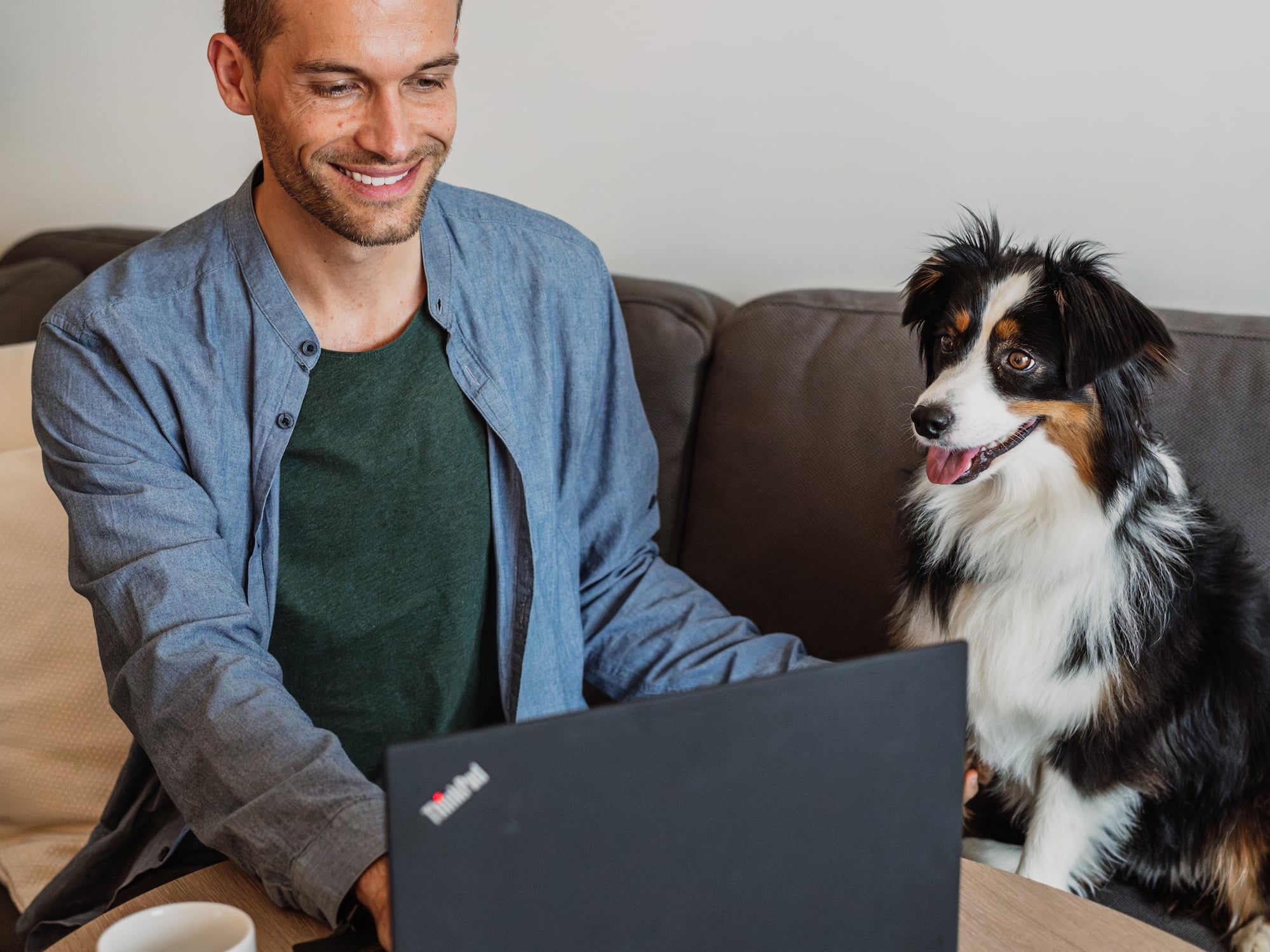 a man sitting at a table with a laptop and a dog