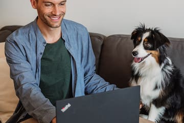 a man sitting at a table with a laptop and a dog