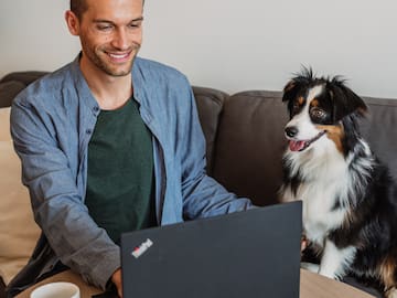 a man sitting at a table with a laptop and a dog