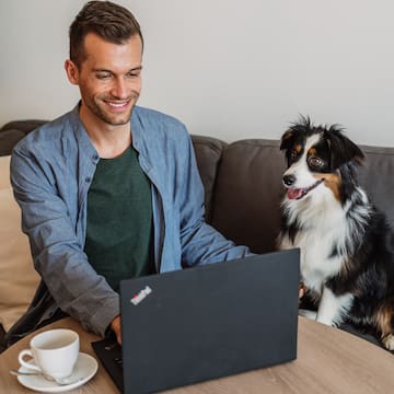 a man sitting at a table with a laptop and a dog