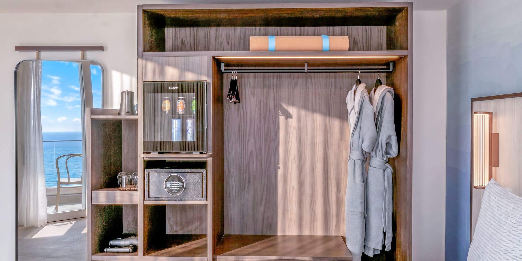 Hotel room wardrobe with minibar, safe, robes, yoga mat. Ocean view mirror.