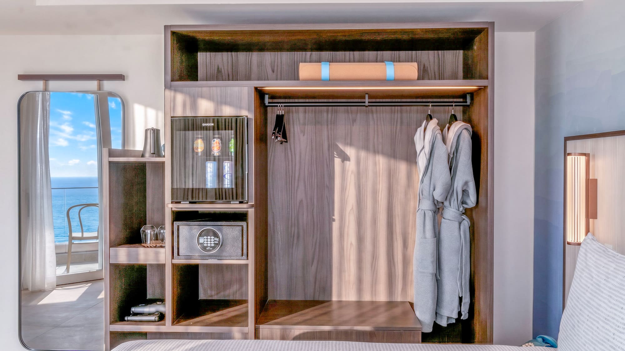 Hotel room wardrobe with minibar, safe, robes, yoga mat. Ocean view mirror.