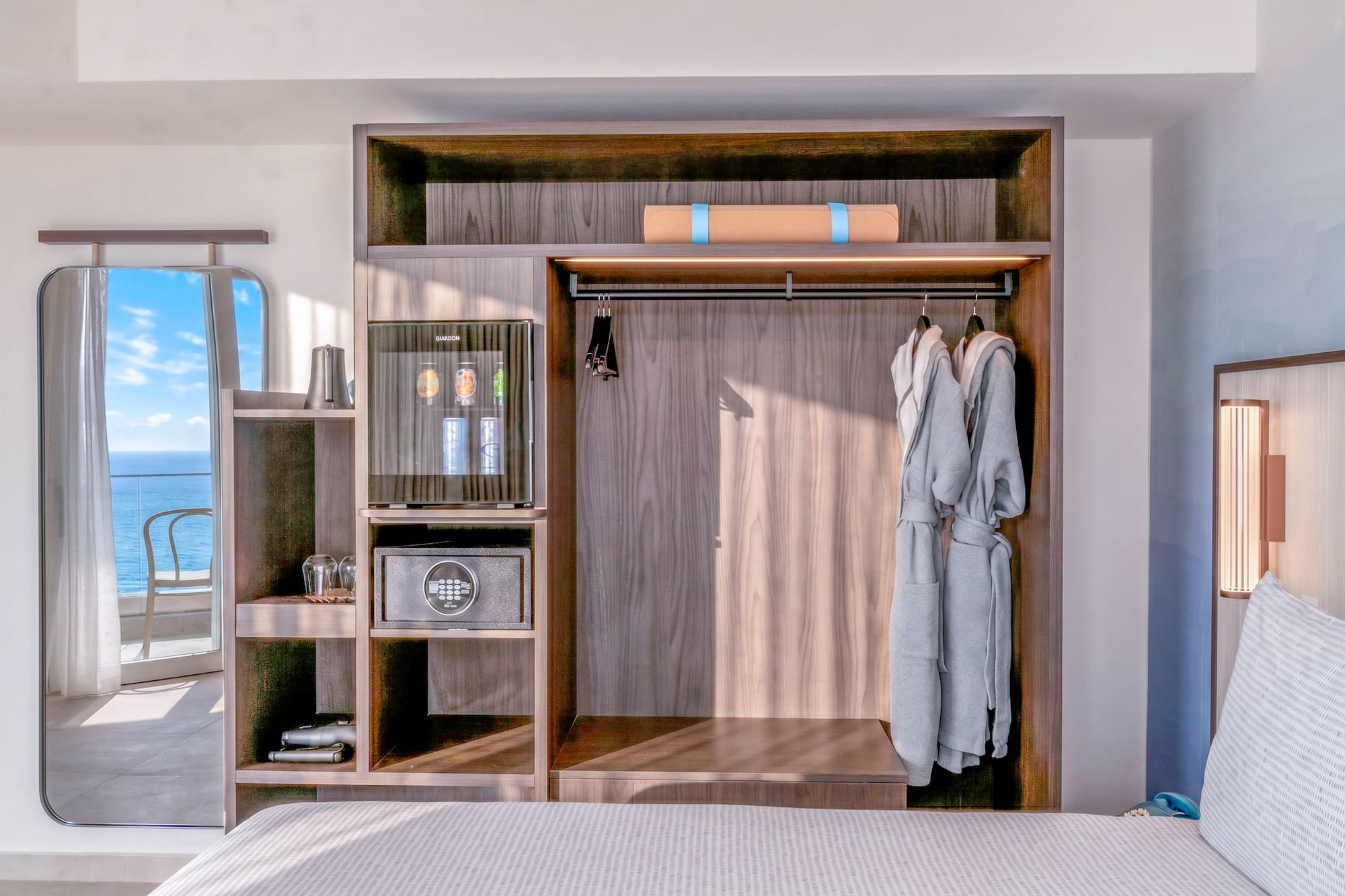 Hotel room wardrobe with minibar, safe, robes, yoga mat. Ocean view mirror.