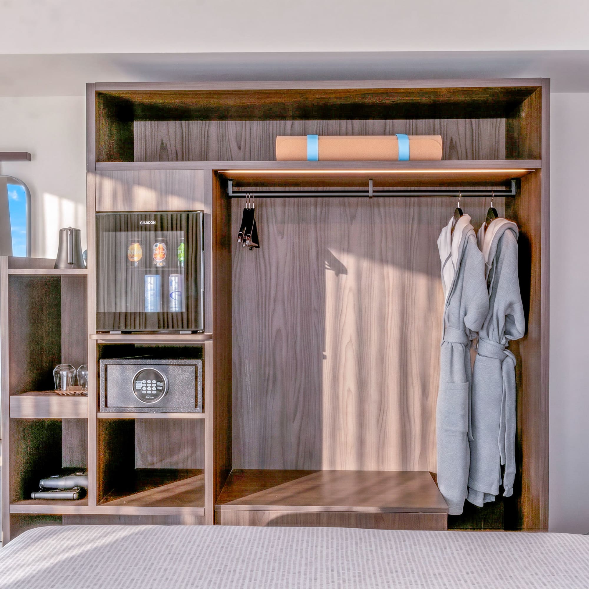 Hotel room wardrobe with minibar, safe, robes, yoga mat. Ocean view mirror.