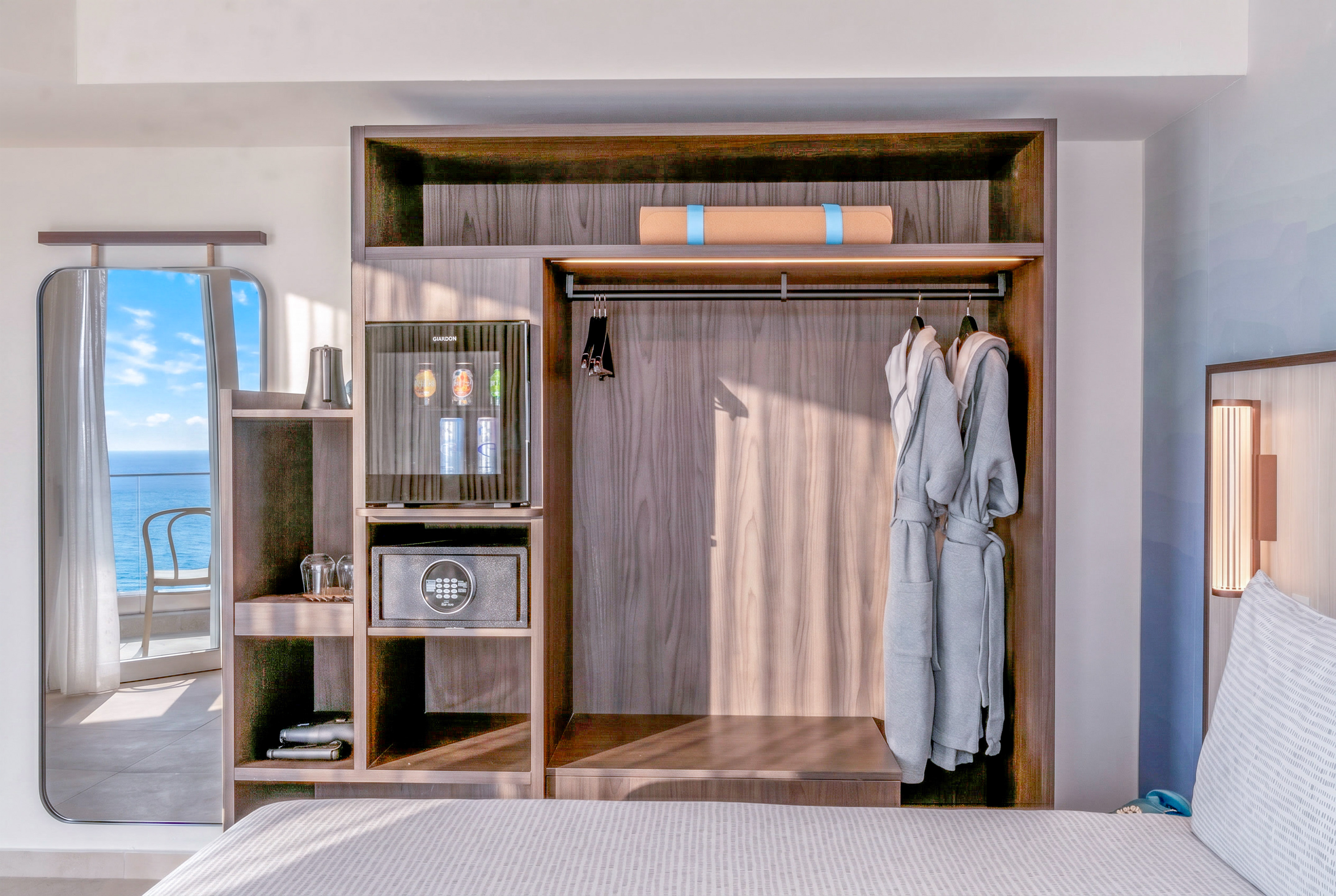 Hotel room wardrobe with minibar, safe, robes, yoga mat. Ocean view mirror.