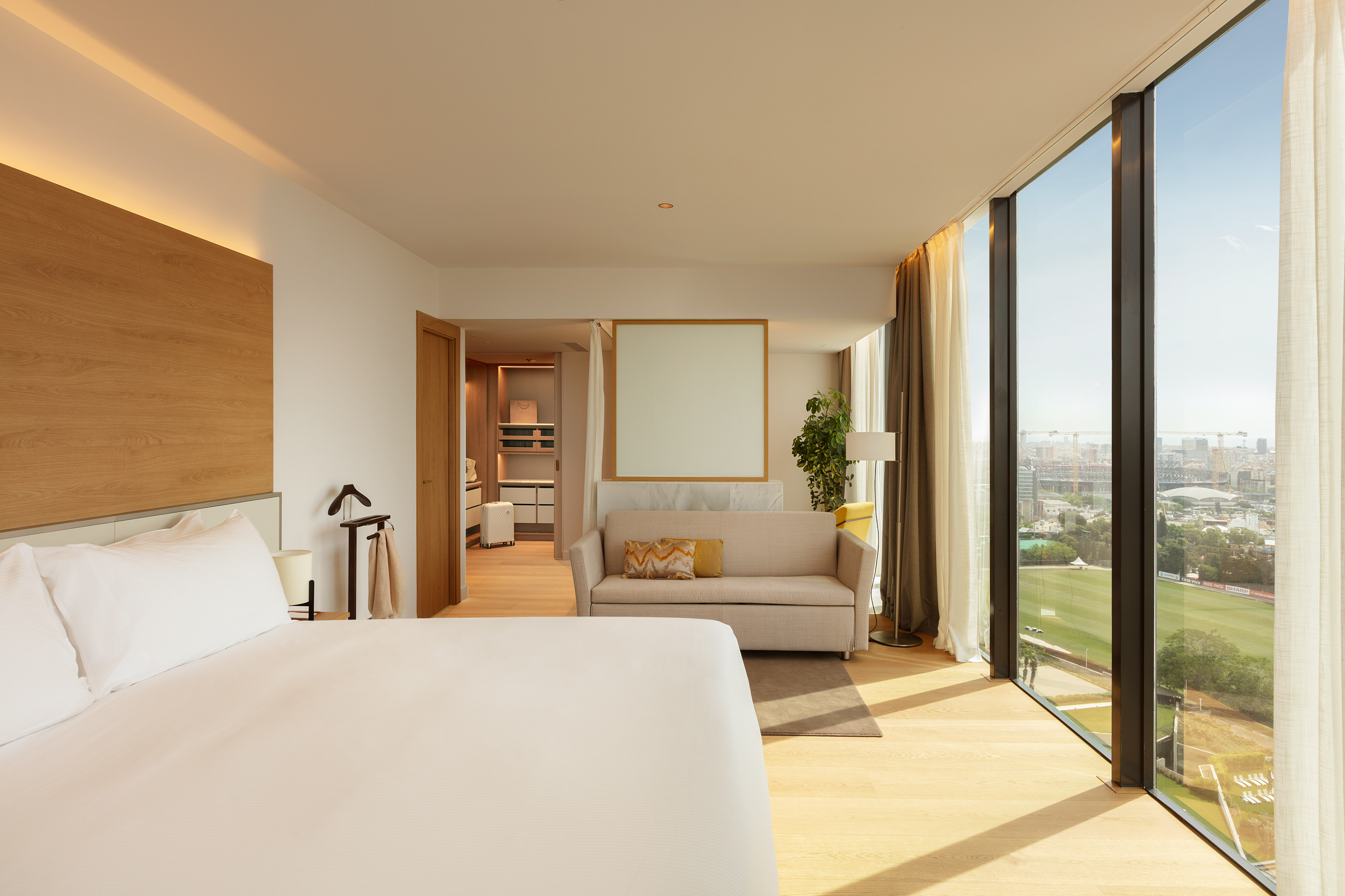 Modern hotel suite with city and stadium views, bed, and sofa.