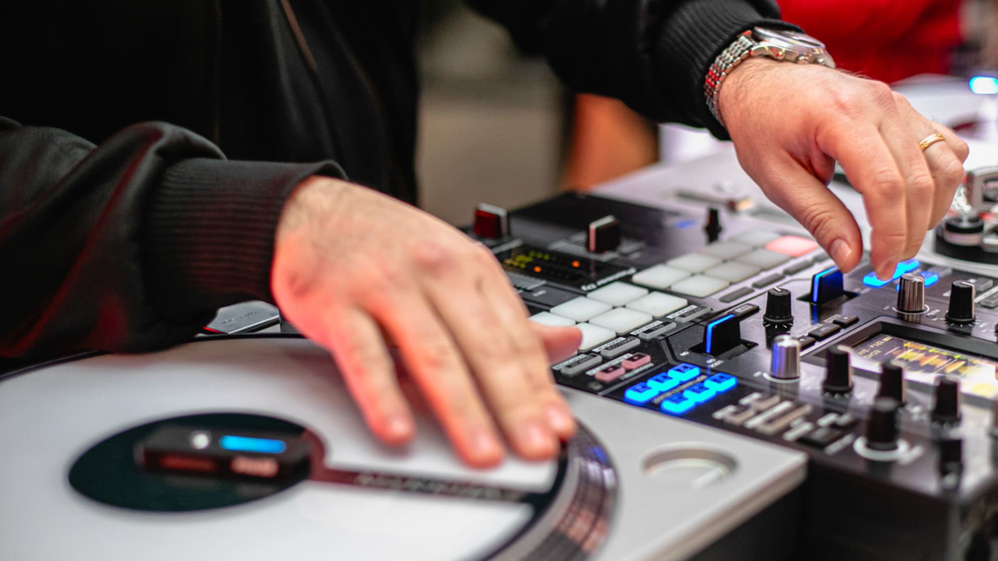 DJ's hands mixing music on a turntable and illuminated audio controller.