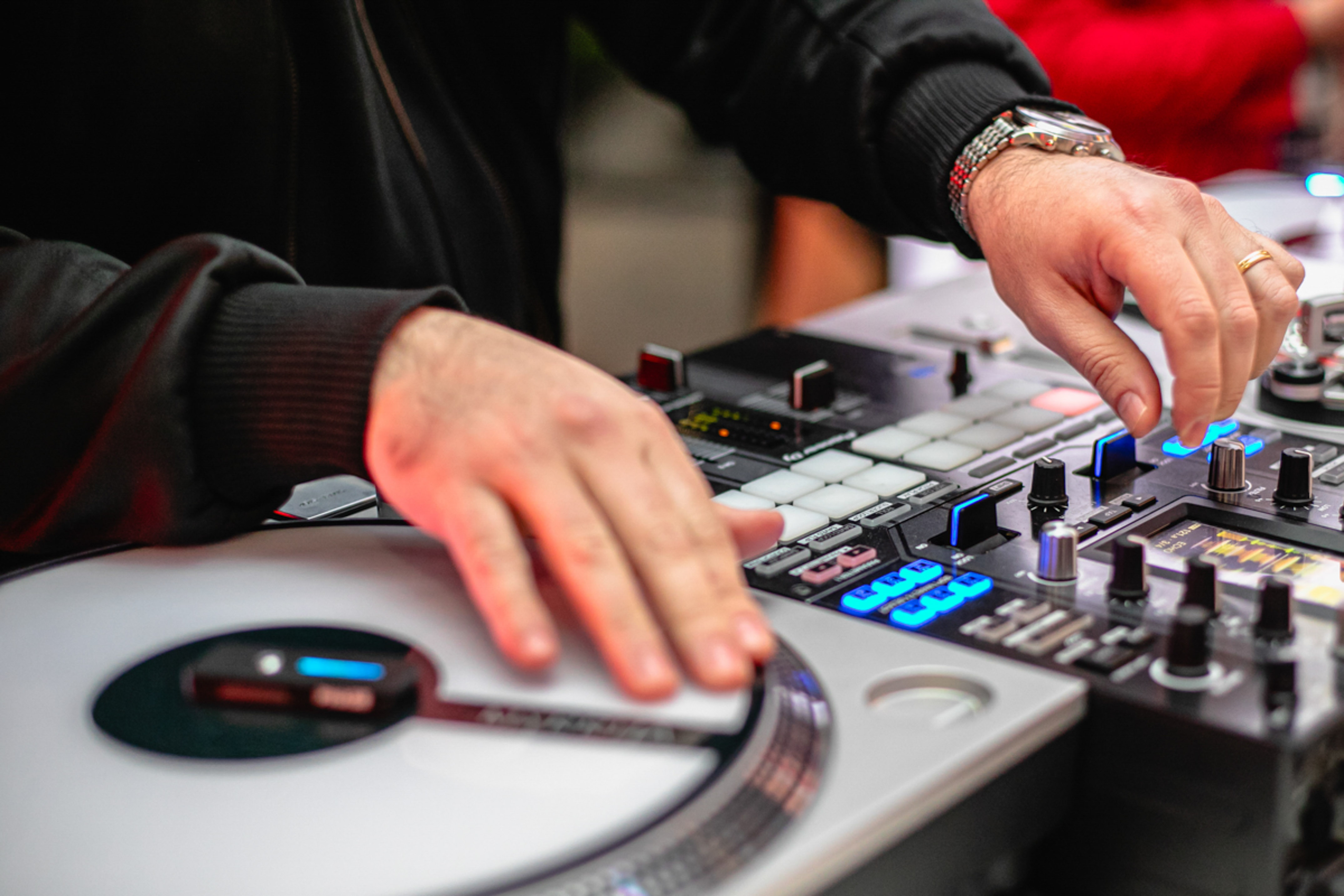 DJ's hands mixing music on a turntable and illuminated audio controller.