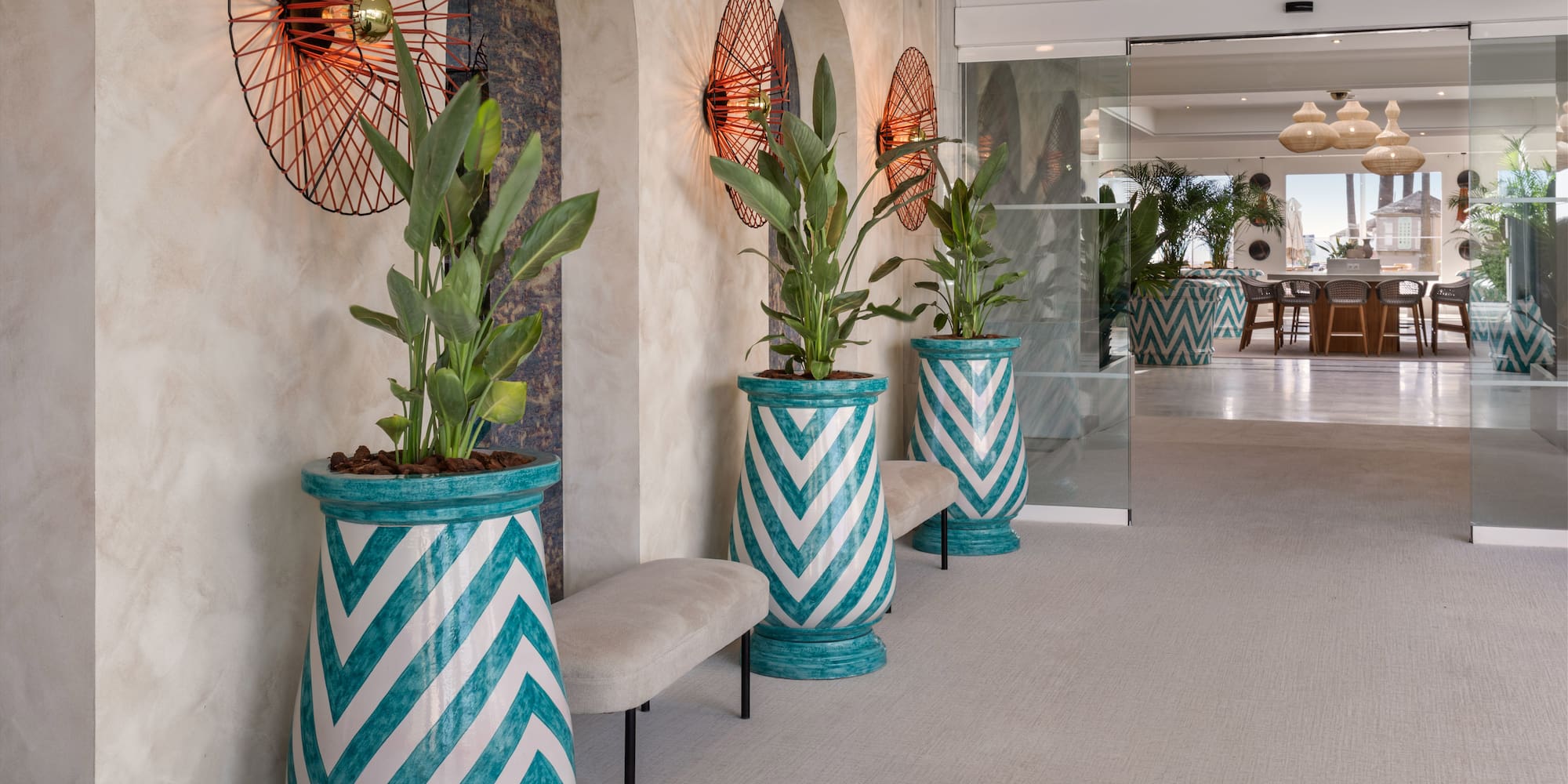 Hotel lobby with teal chevron planters, lush green plants, and modern wall sconces.