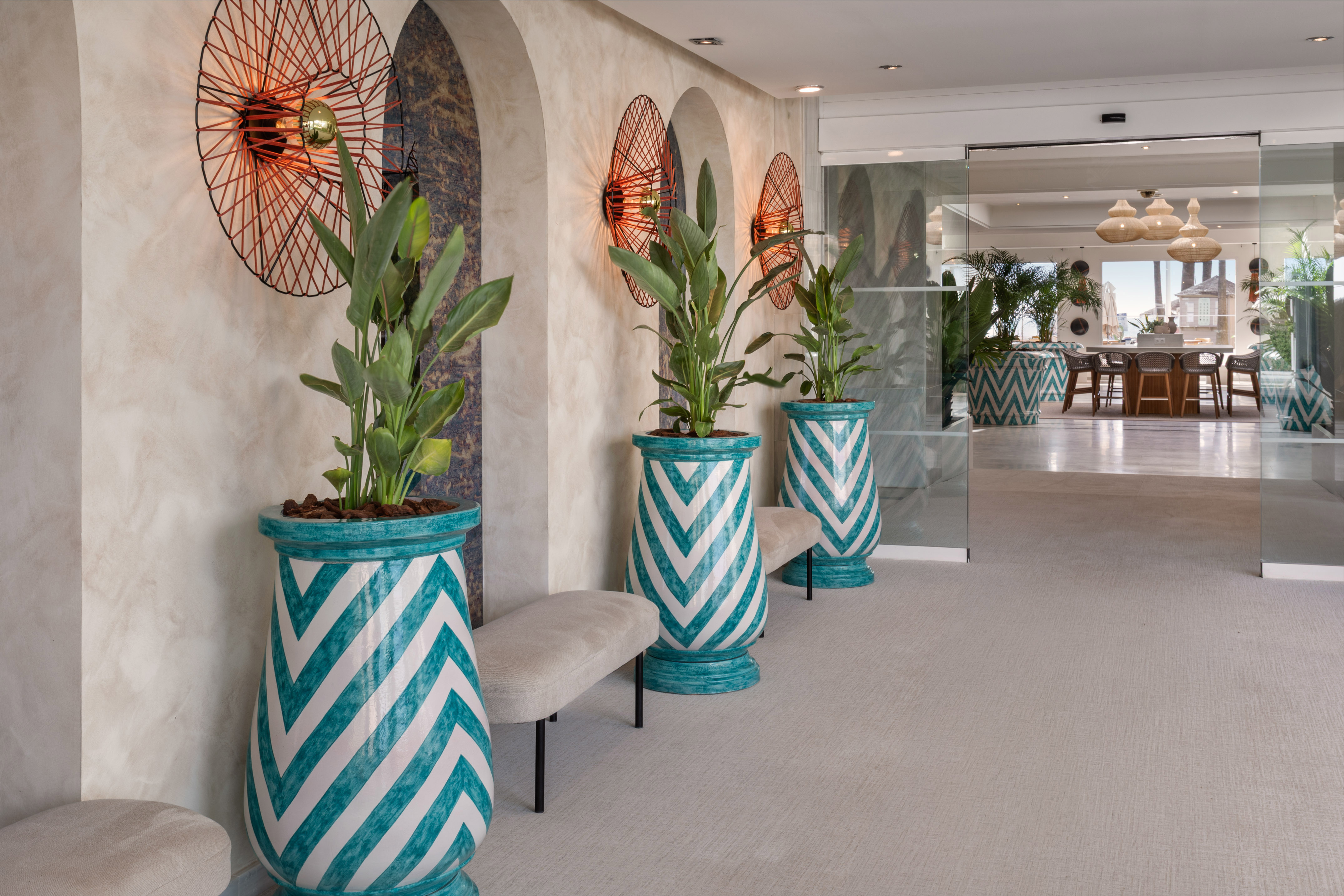 Hotel lobby with teal chevron planters, lush green plants, and modern wall sconces.