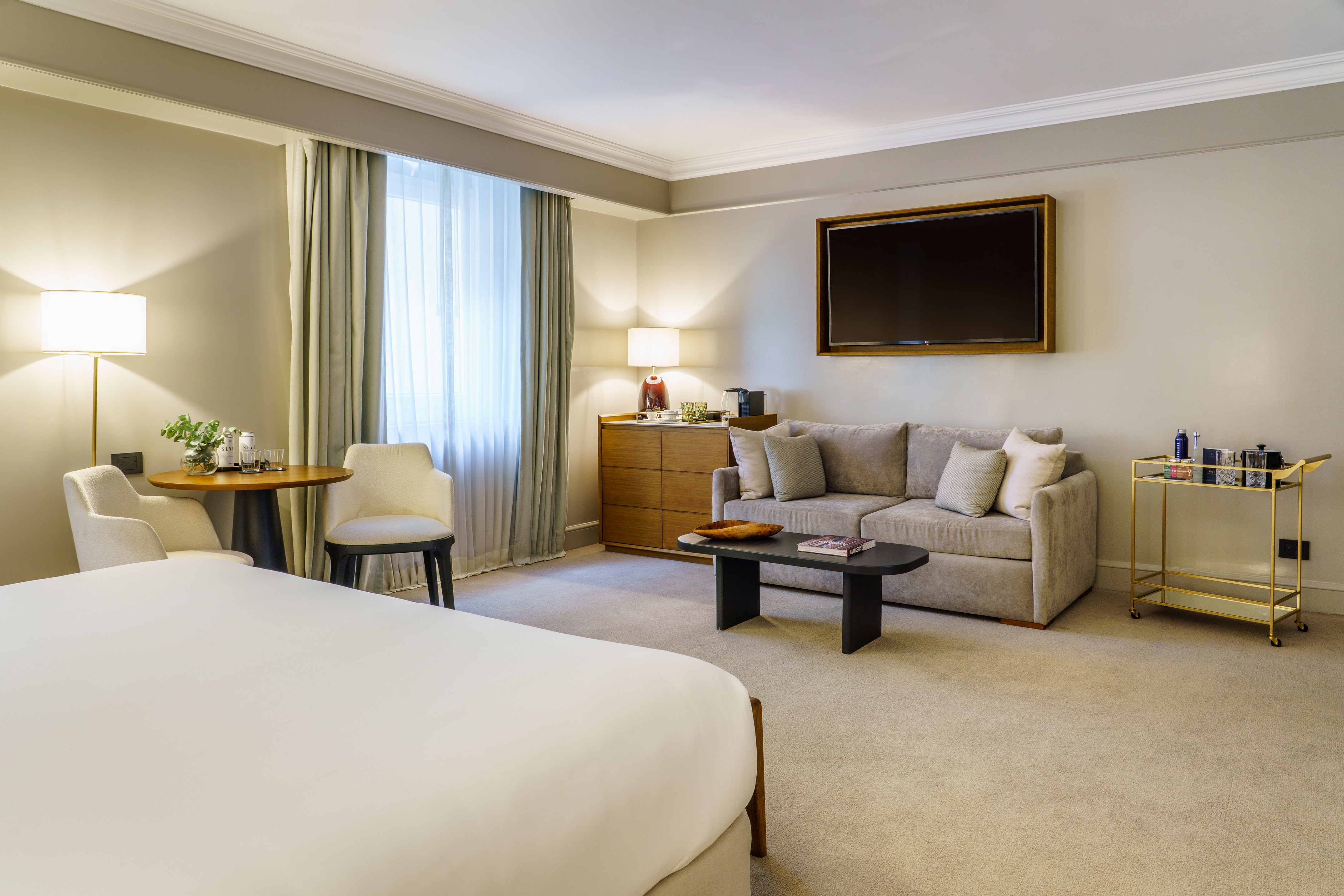 Luxury hotel suite with bed, sofa, TV, and dining area.