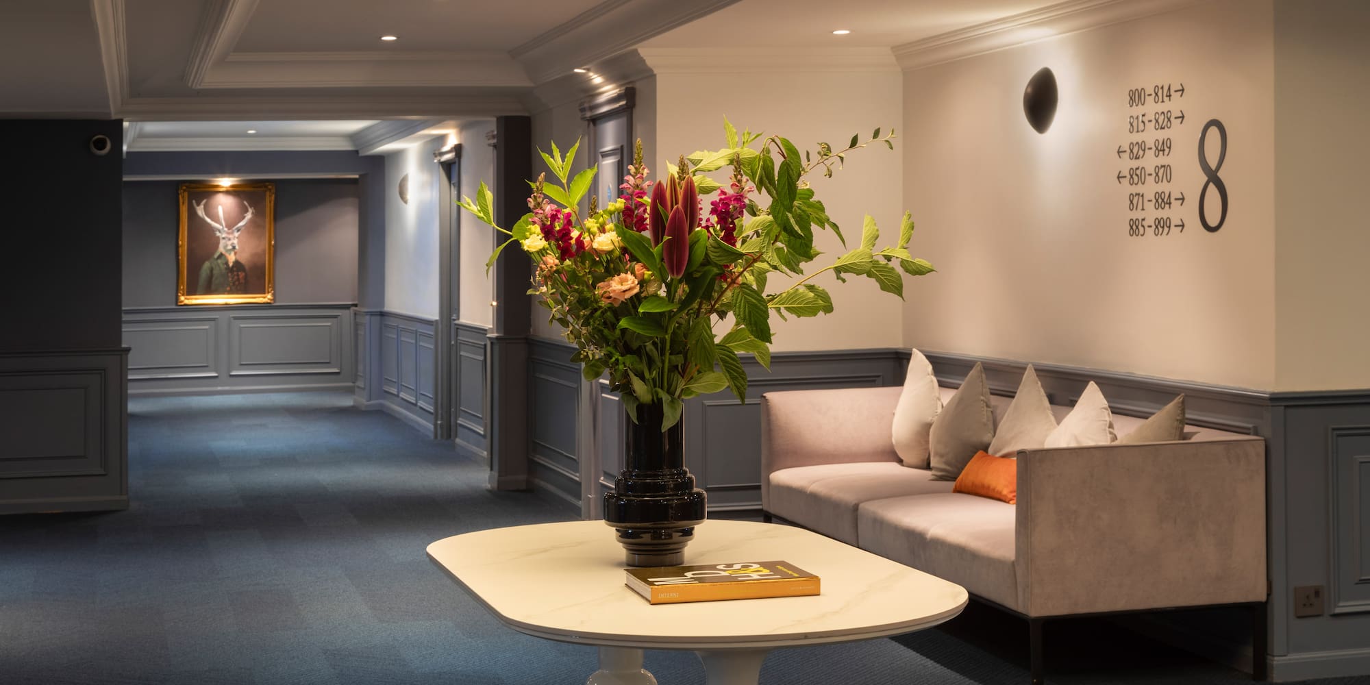 Elegant hotel lobby with floral arrangement, sofa, and deer painting.