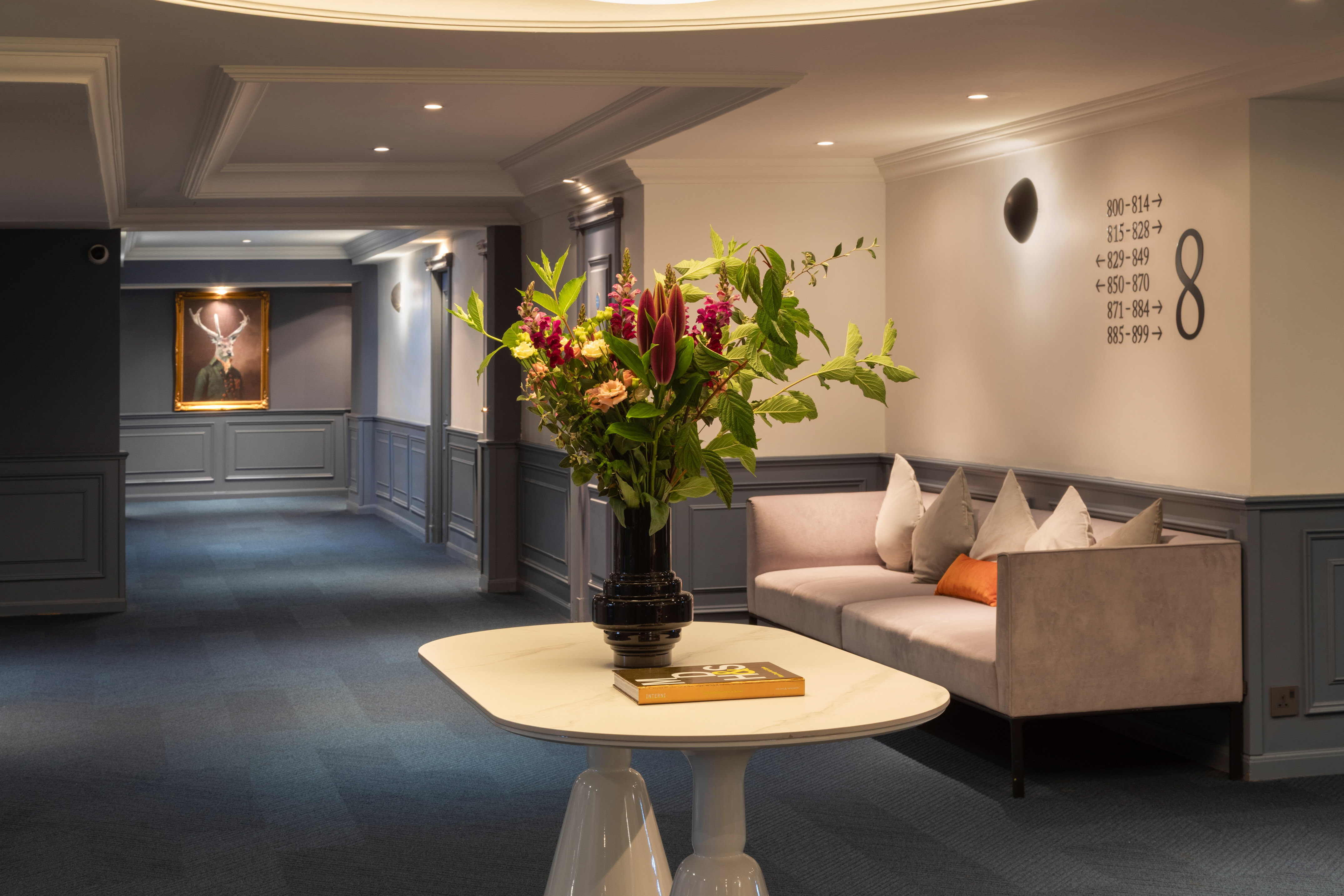 Elegant hotel lobby with floral arrangement, sofa, and deer painting.