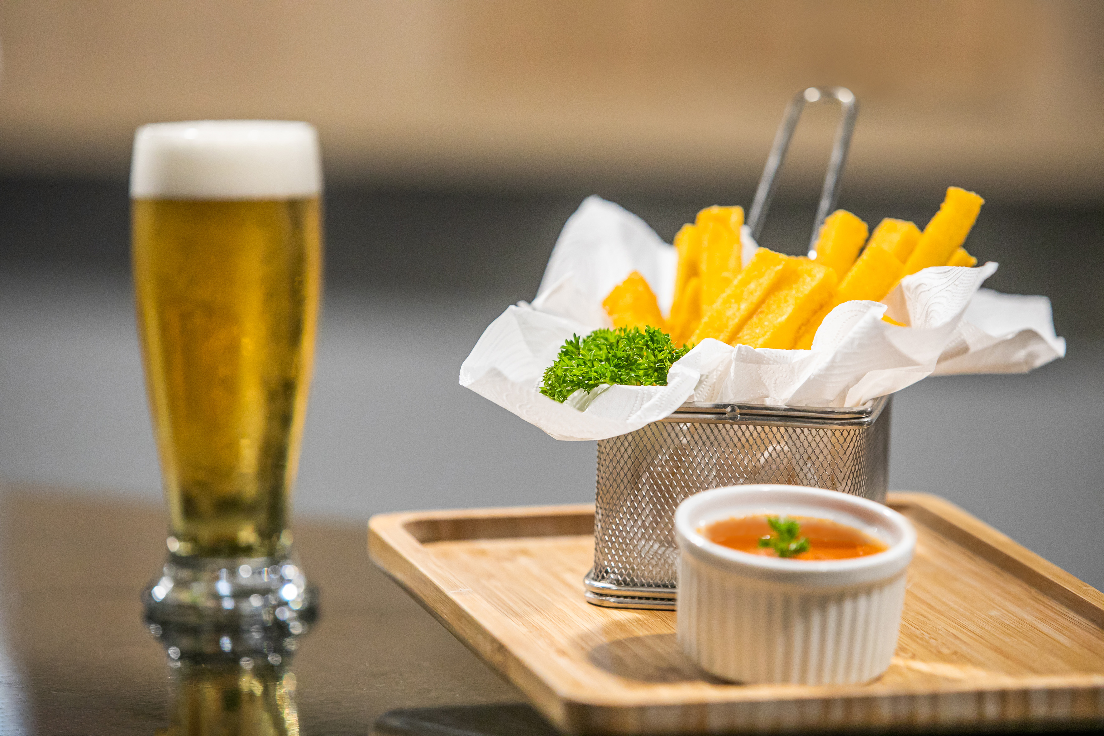 Golden fries, dipping sauce, and a beer on a wooden tray.