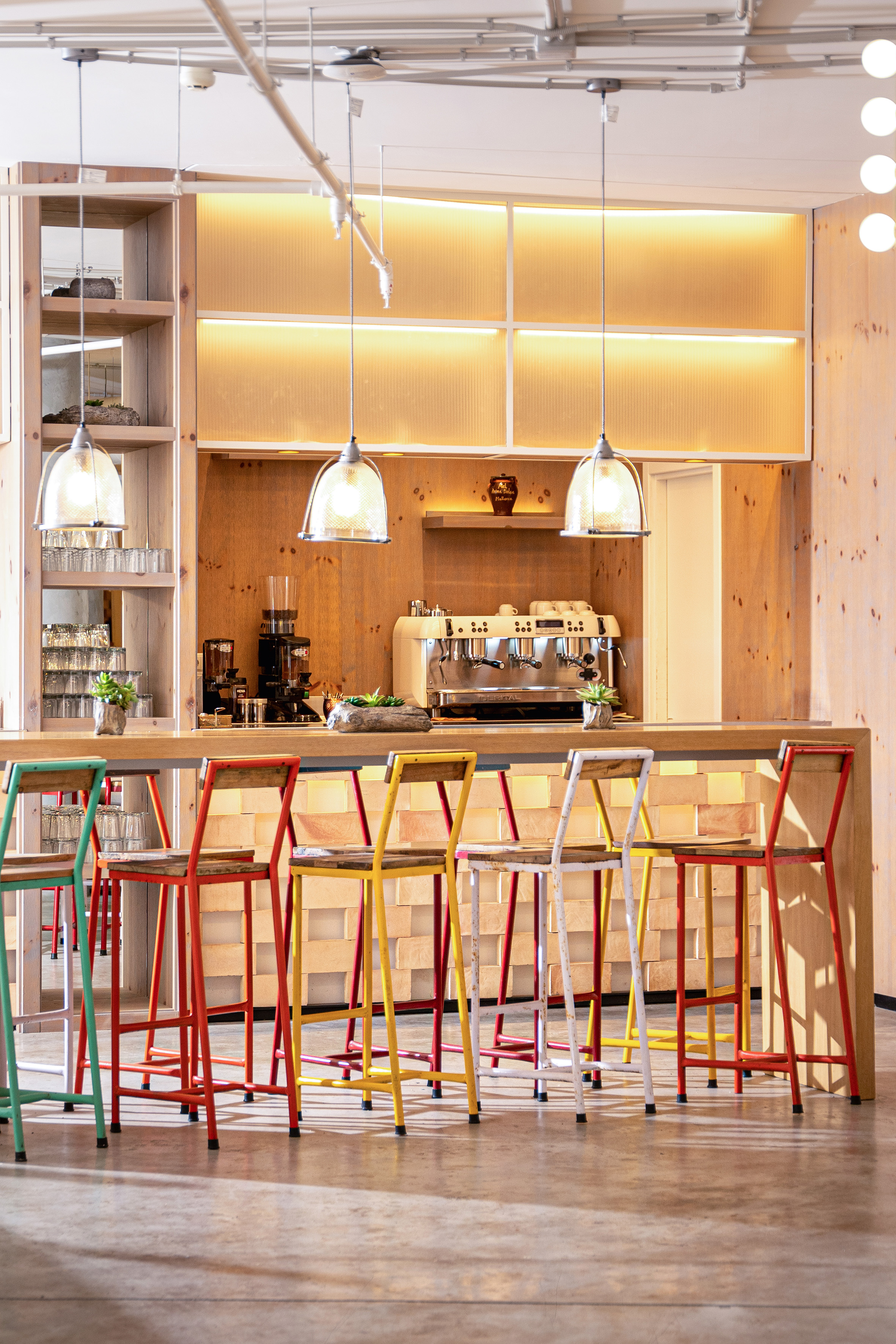 Modern wooden coffee bar with colorful stools and espresso machine.