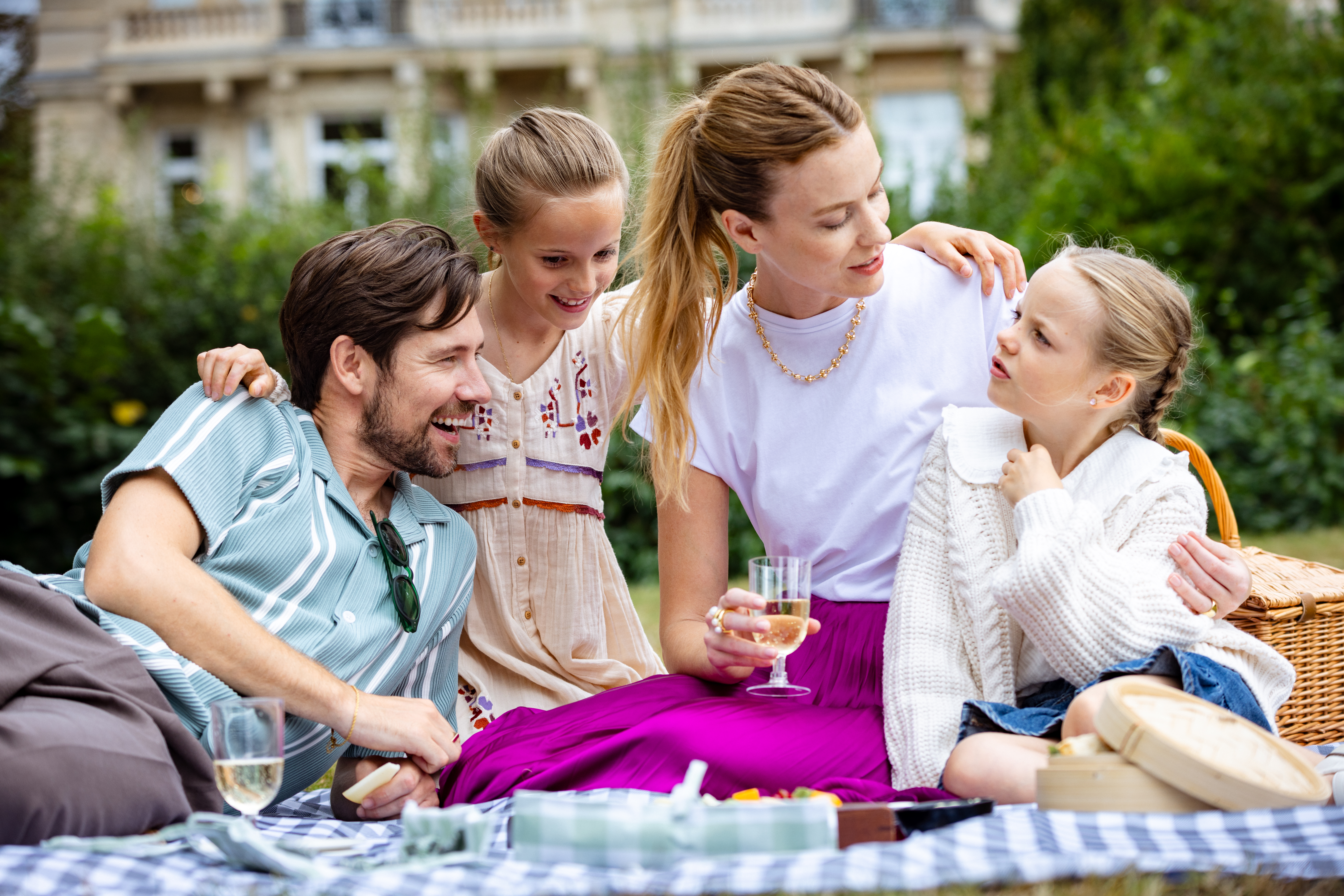 Familia de picnic en parque, manta a cuadros, bebidas, césped verde.