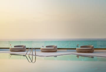 Luxury pool deck with three daybeds overlooking the ocean at sunset.