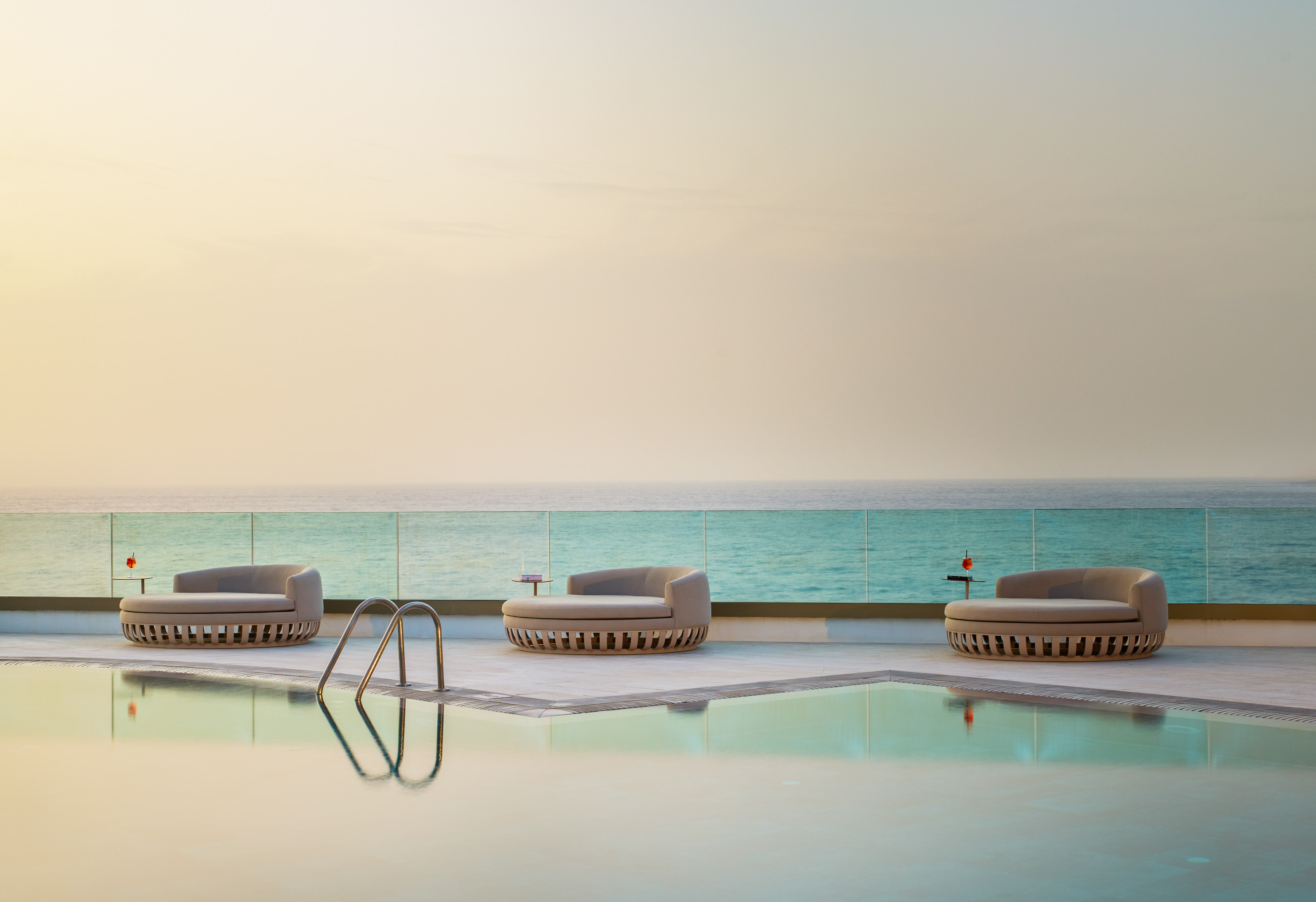 Luxury pool deck with three daybeds overlooking the ocean at sunset.