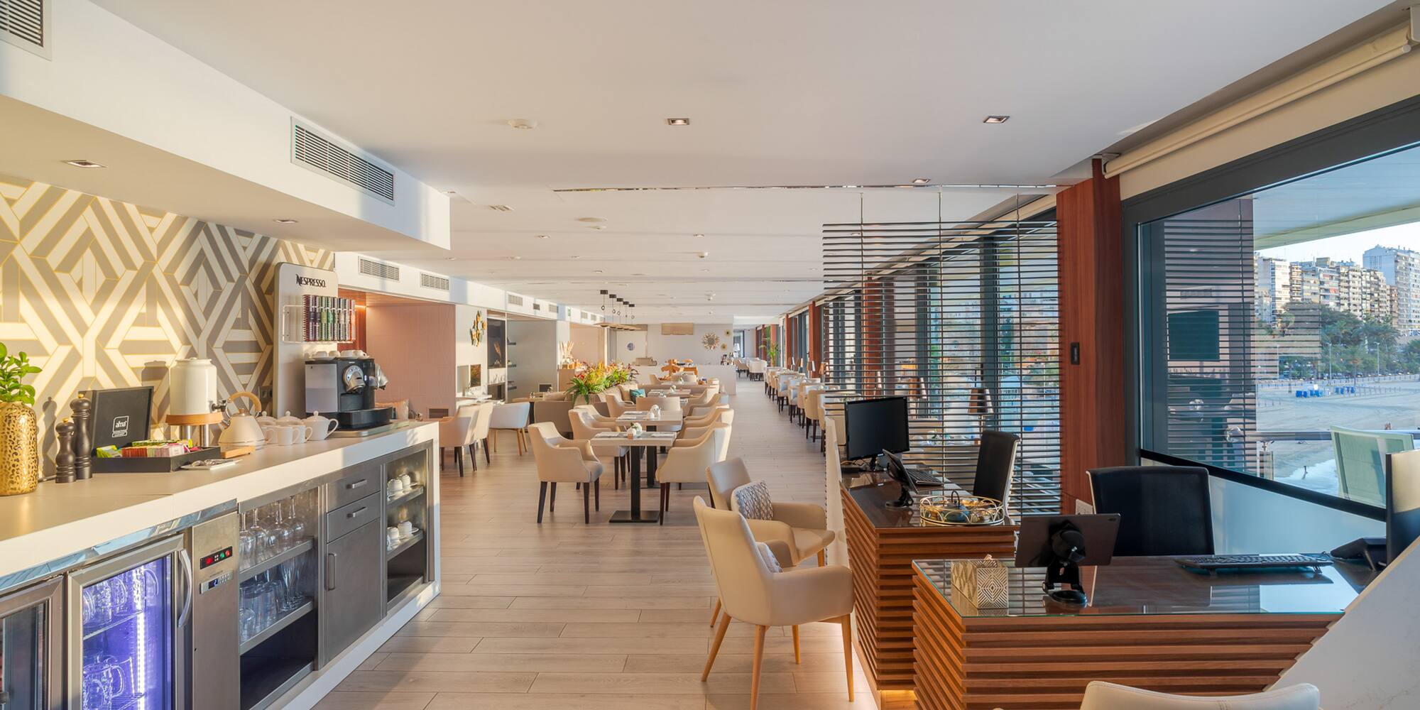 Bright hotel restaurant, Nespresso station, dining tables, city views.