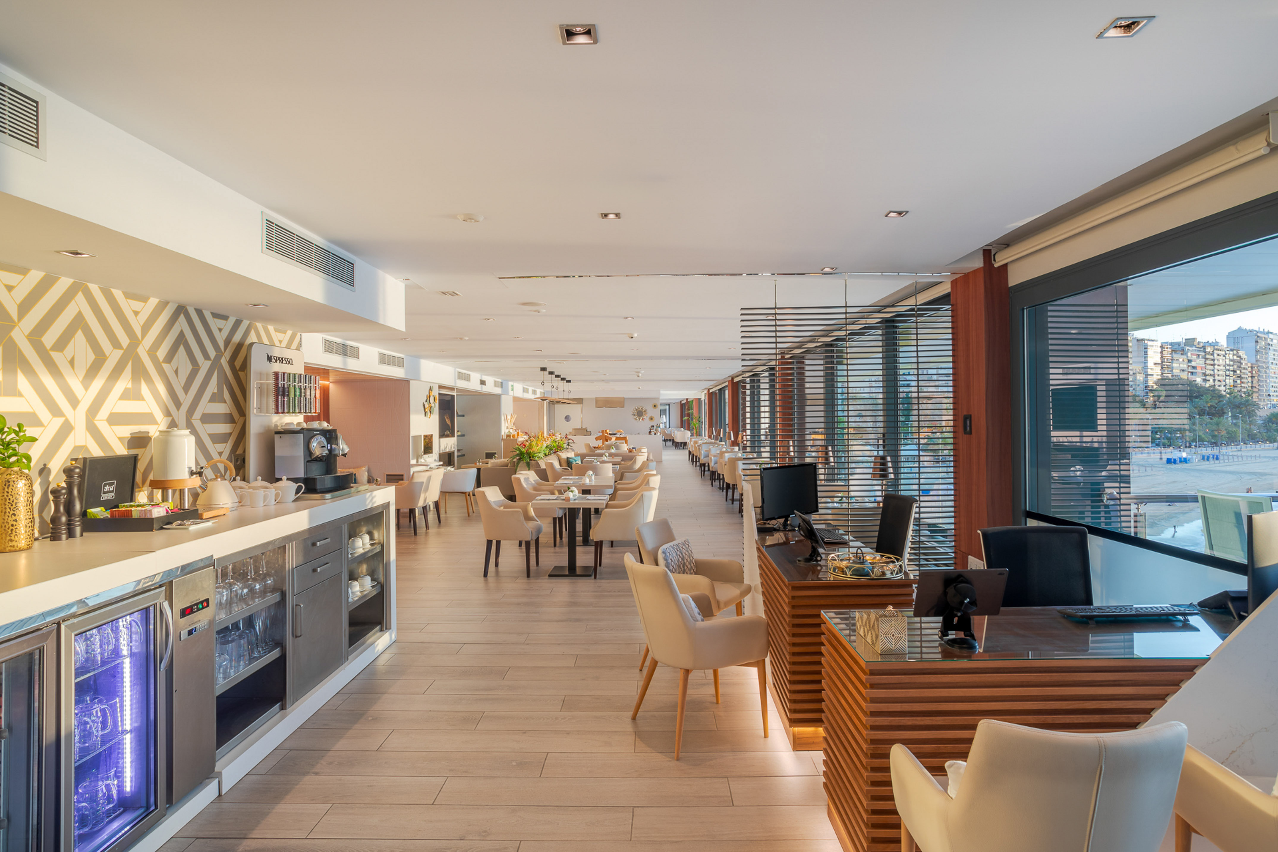 Bright hotel restaurant, Nespresso station, dining tables, city views.