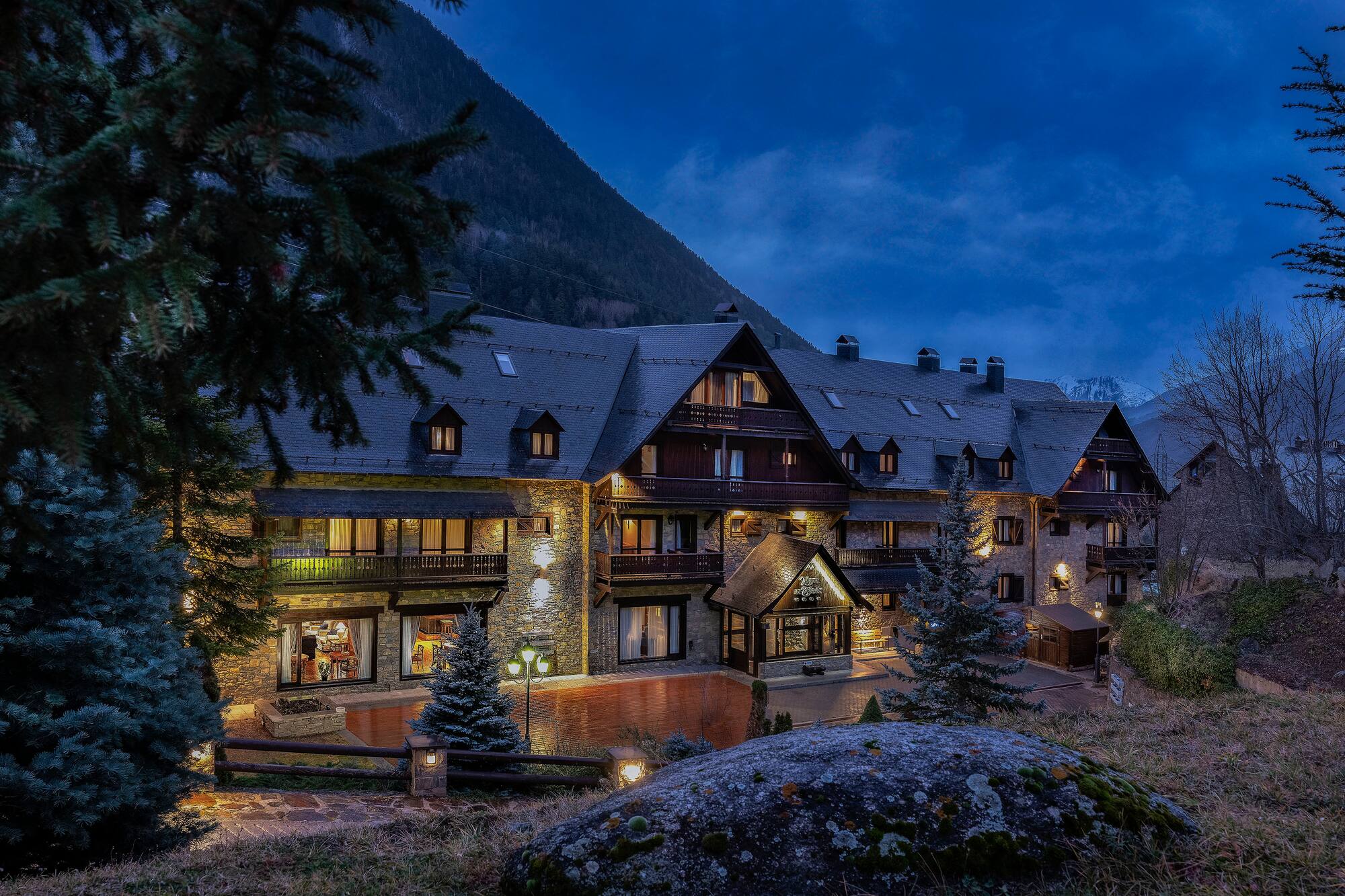 Illuminated stone mountain lodge at dusk, nestled among pine trees.