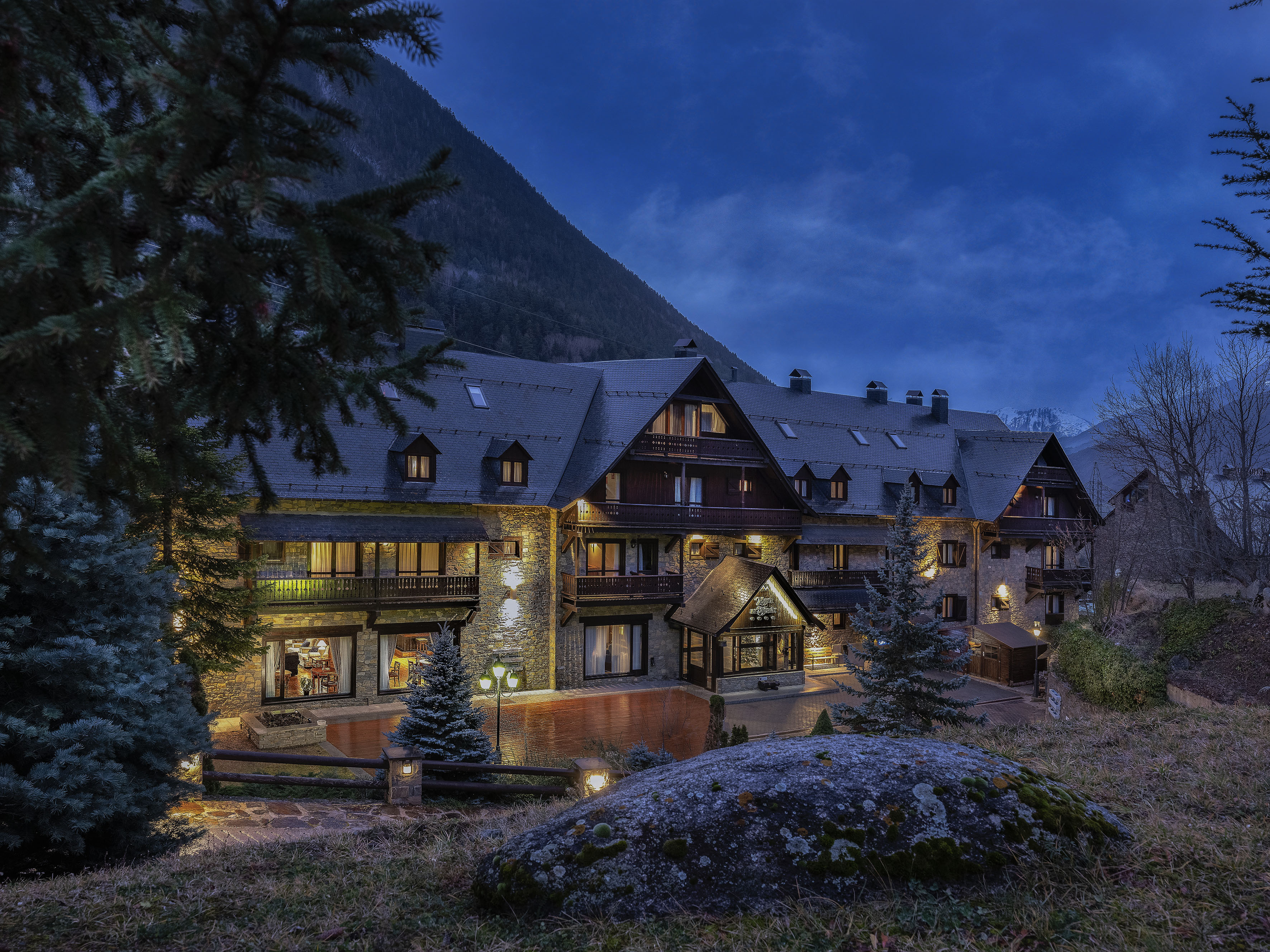 Illuminated stone mountain lodge at dusk, nestled among pine trees.