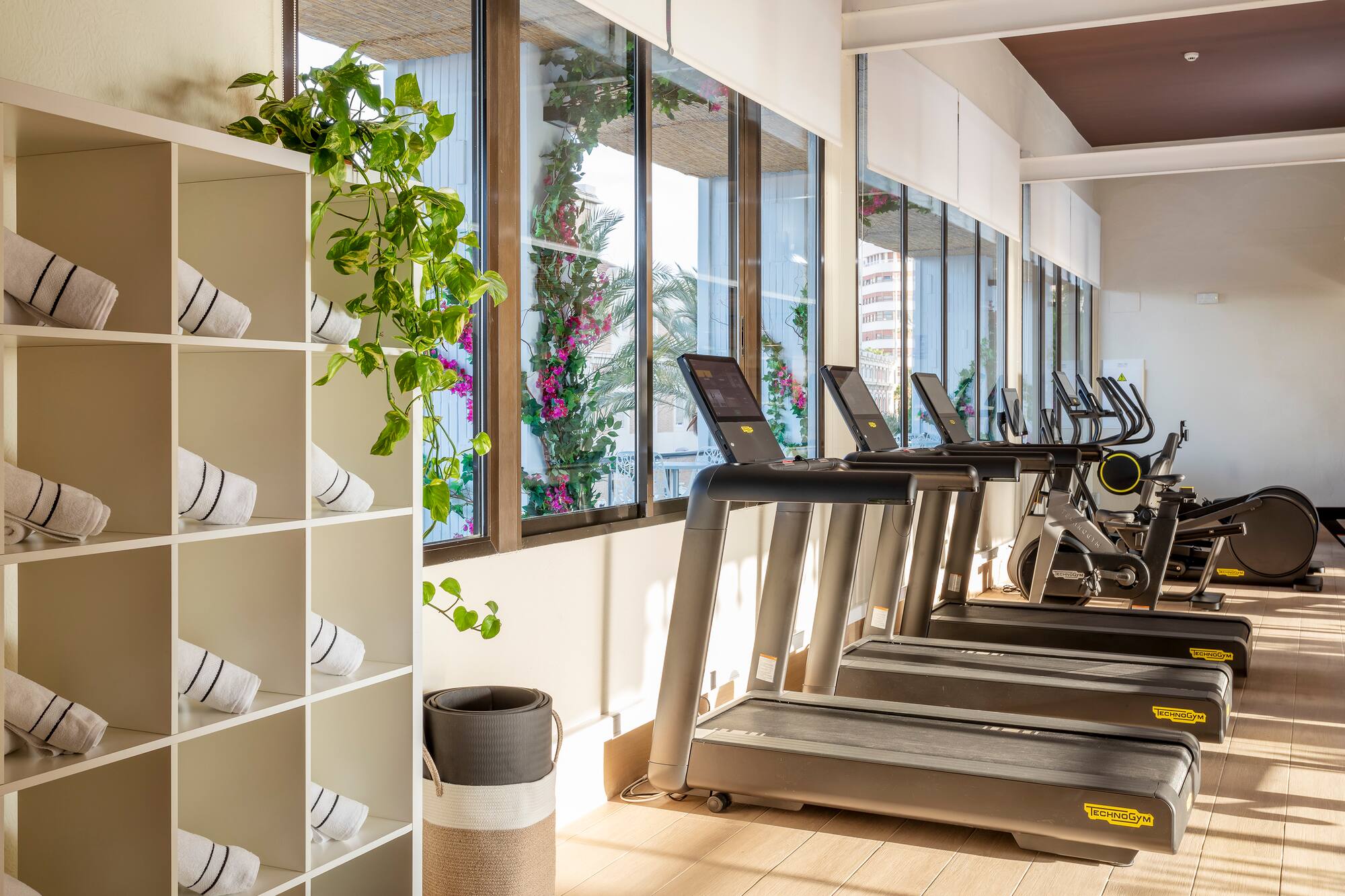 Modern gym with Technogym treadmills, towels, and lush garden views.