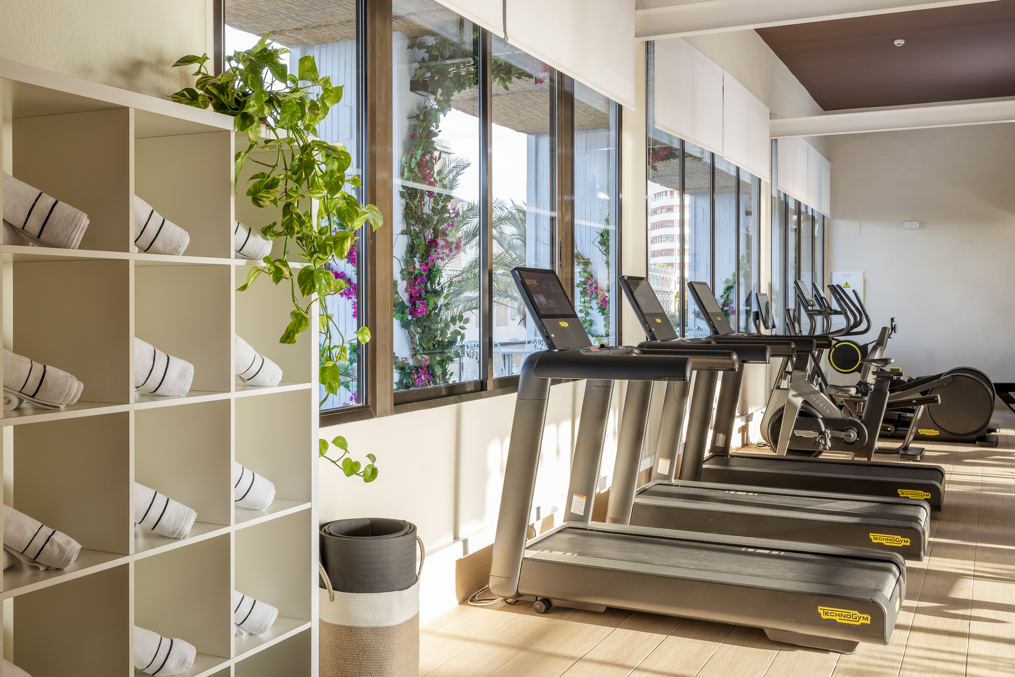 Modern gym with Technogym treadmills, towels, and lush garden views.