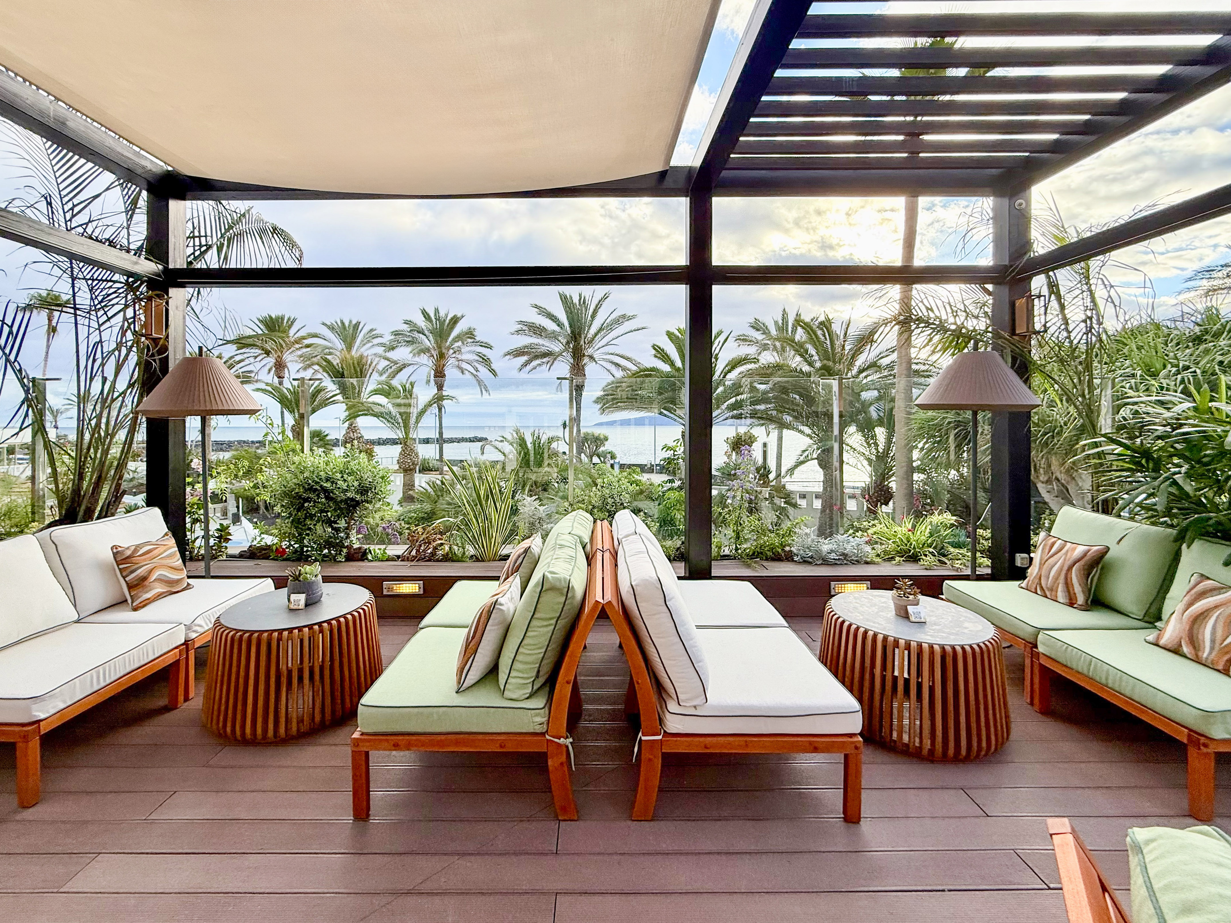 Tropical outdoor lounge with modern furniture, palm trees, and ocean view.