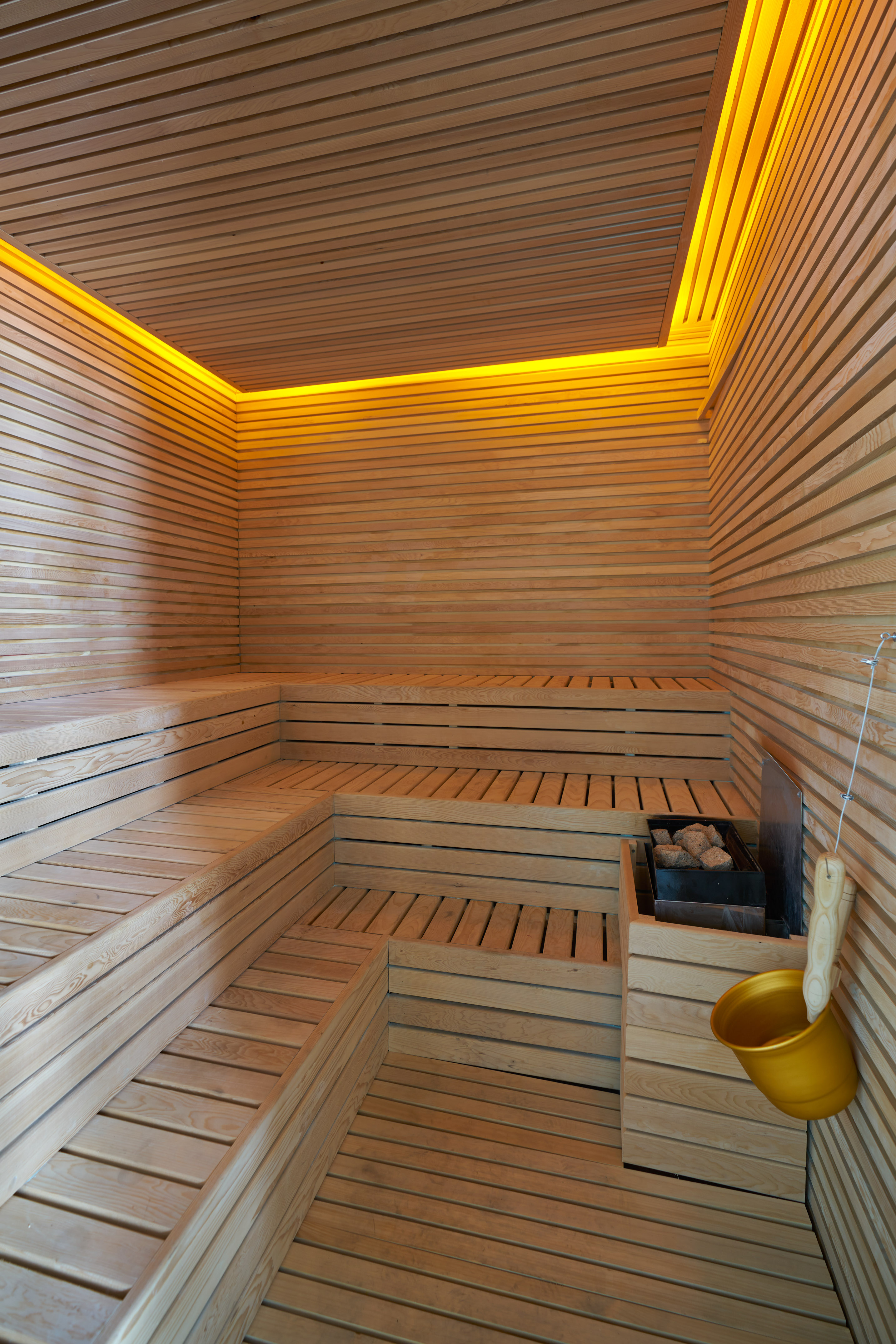 Modern wooden sauna room with tiered benches, heater, and warm lighting for spa.