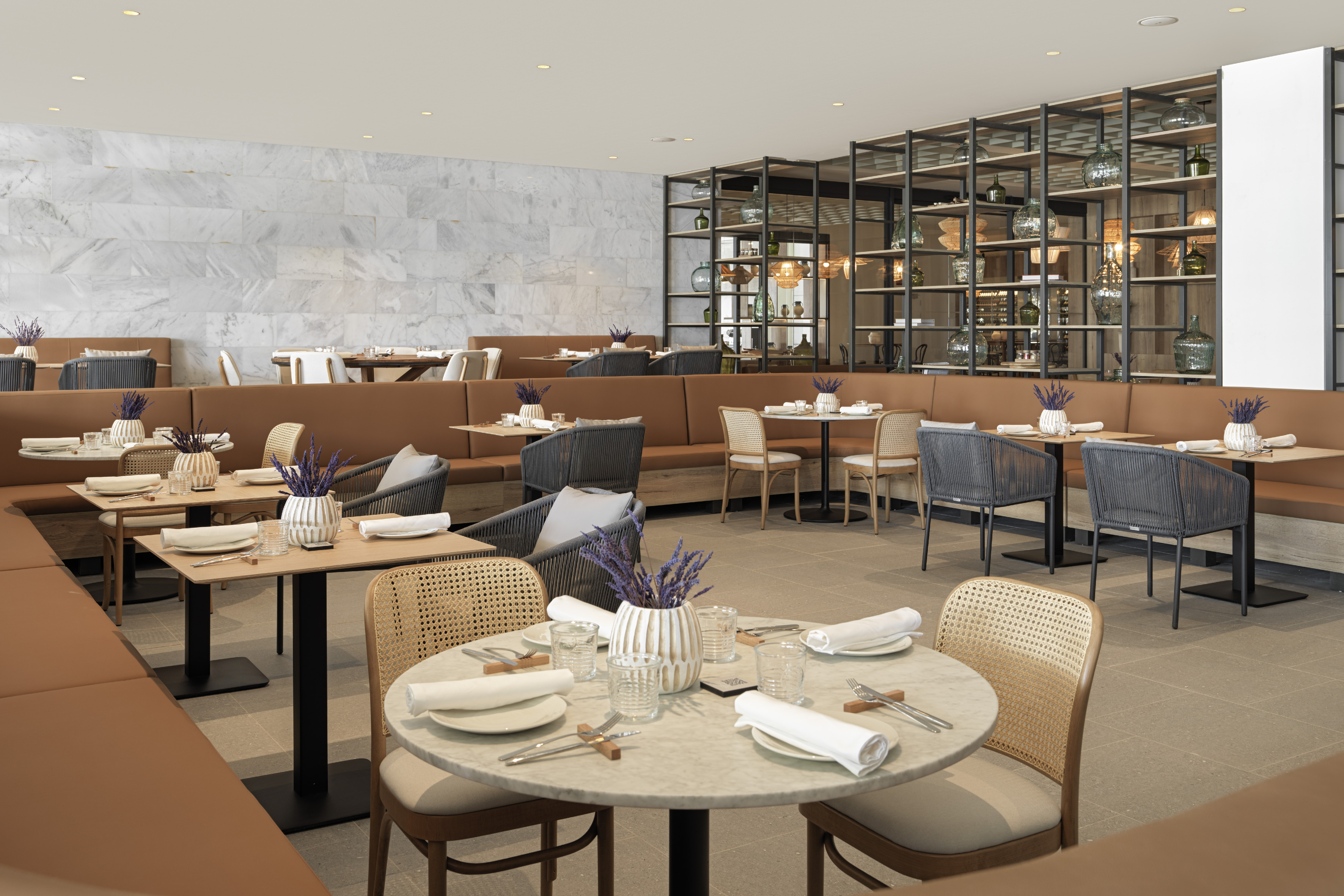 Modern restaurant dining room with marble wall, stylish banquettes, and set tables.
