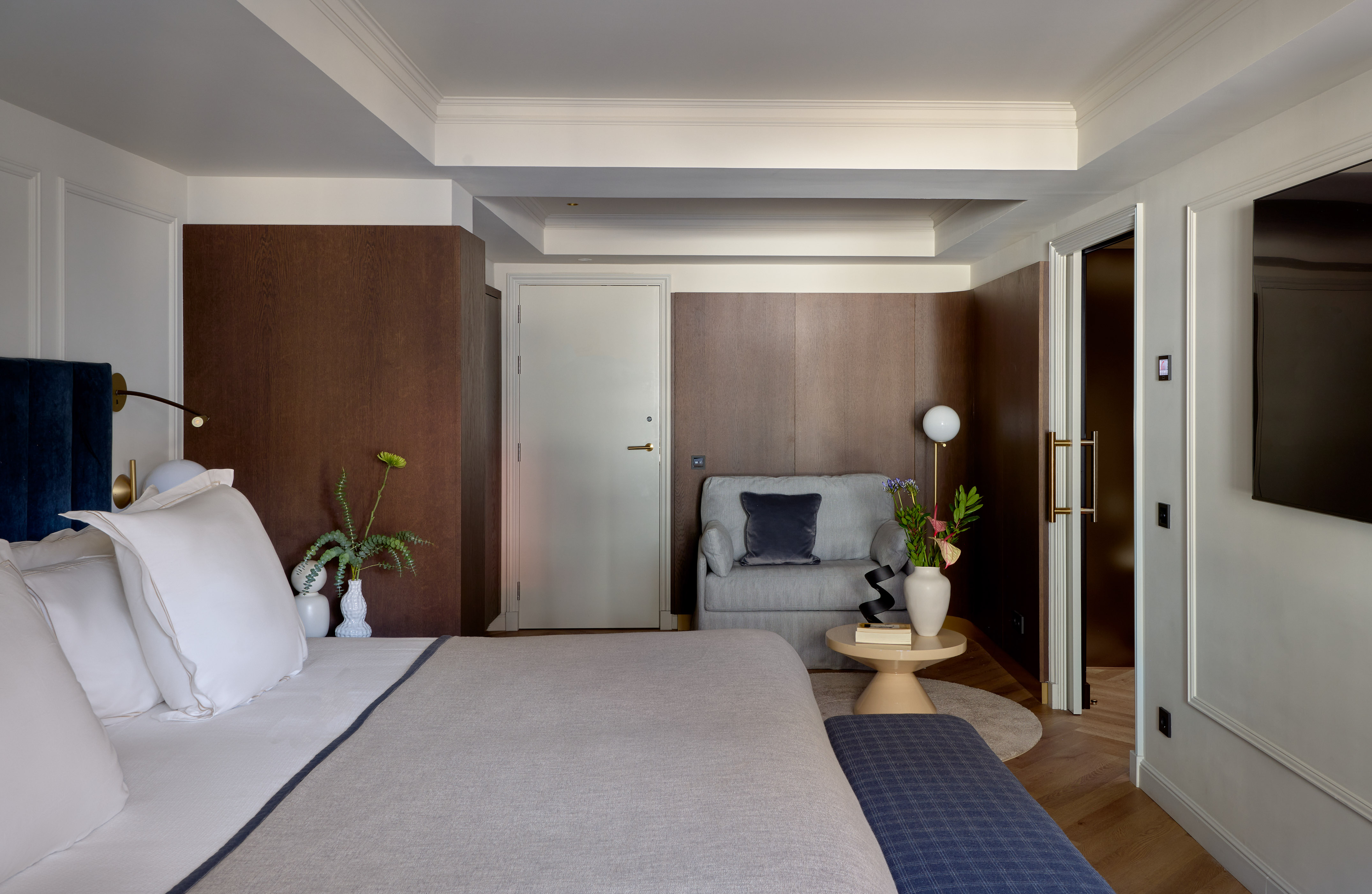 Stylish hotel room featuring a king bed, cozy sofa, and elegant wood paneling.