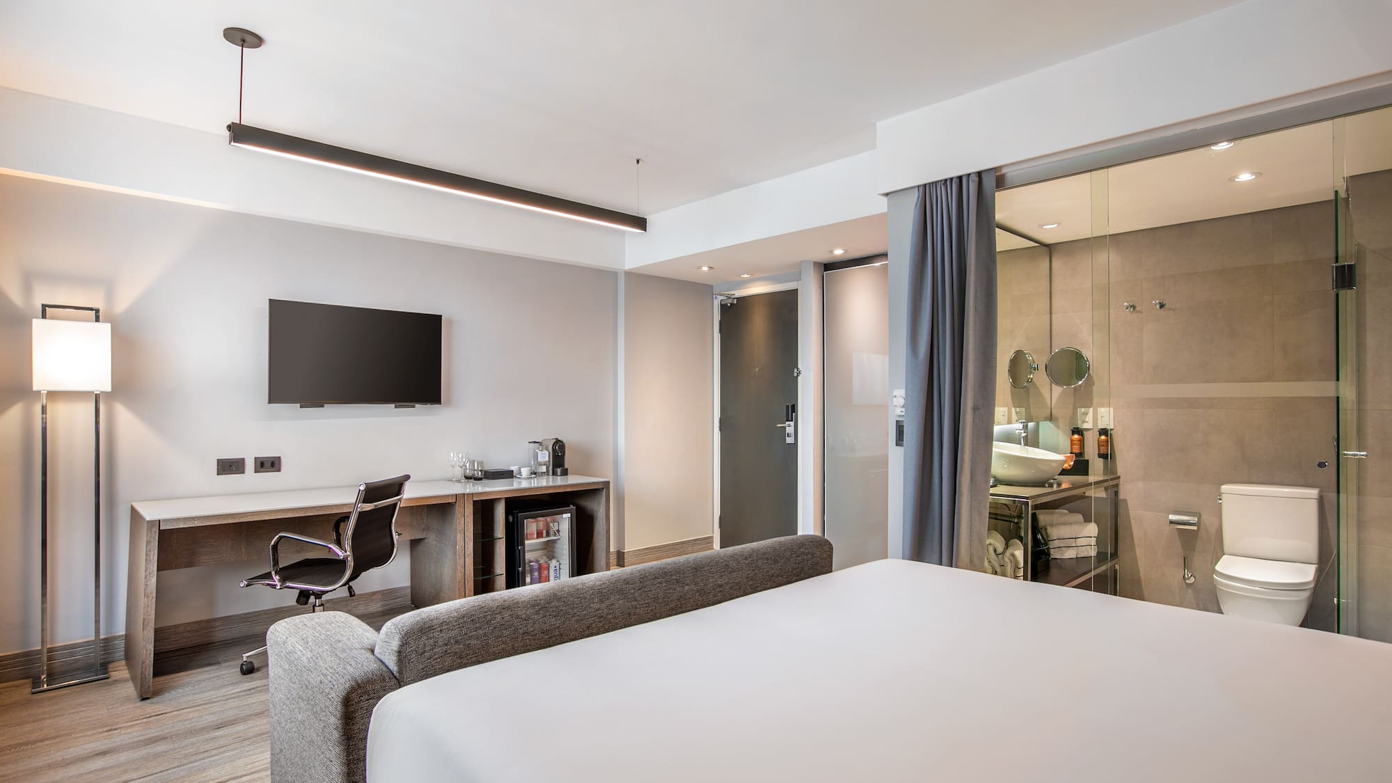 Quarto de hotel moderno com cama, escrivaninha, TV e banheiro de vidro. - Grand Premium - Meliá Ibirapuera, São Paulo