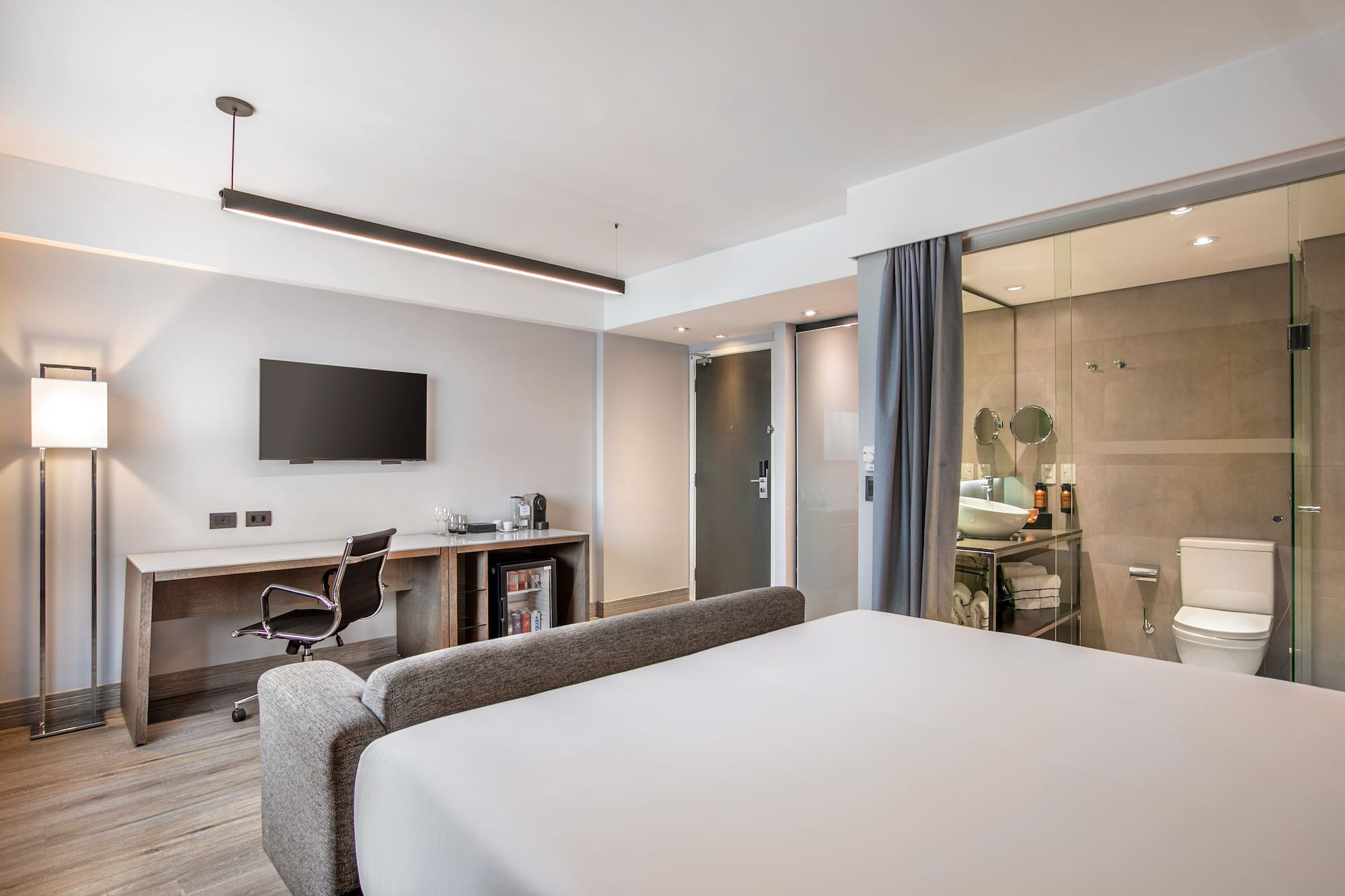 Quarto de hotel moderno com cama, escrivaninha, TV e banheiro de vidro. - Grand Premium - Meliá Ibirapuera, São Paulo